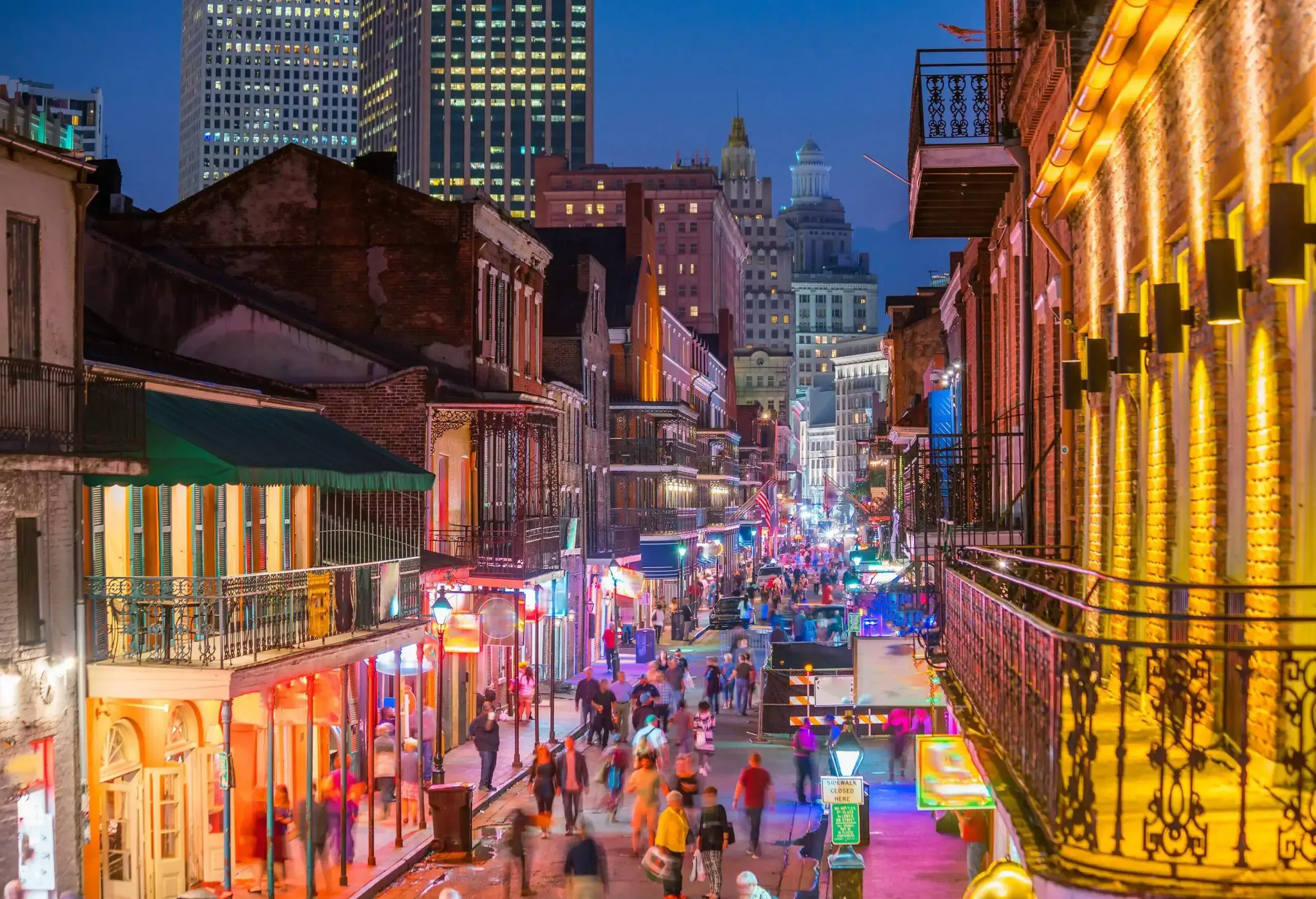 A vibrant avenue coming alive at night with bright lights as people stroll by the stores and restaurants.