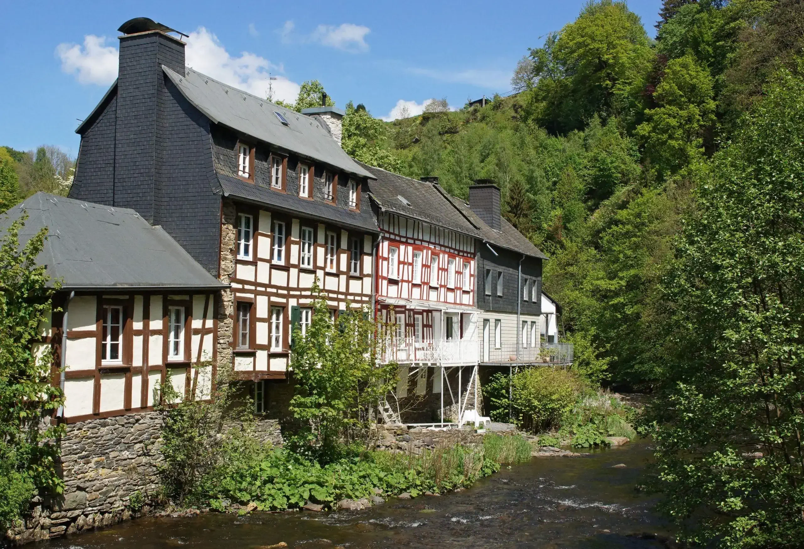 A shallow river flowing alongside timber-framed houses surrounded by trees.
