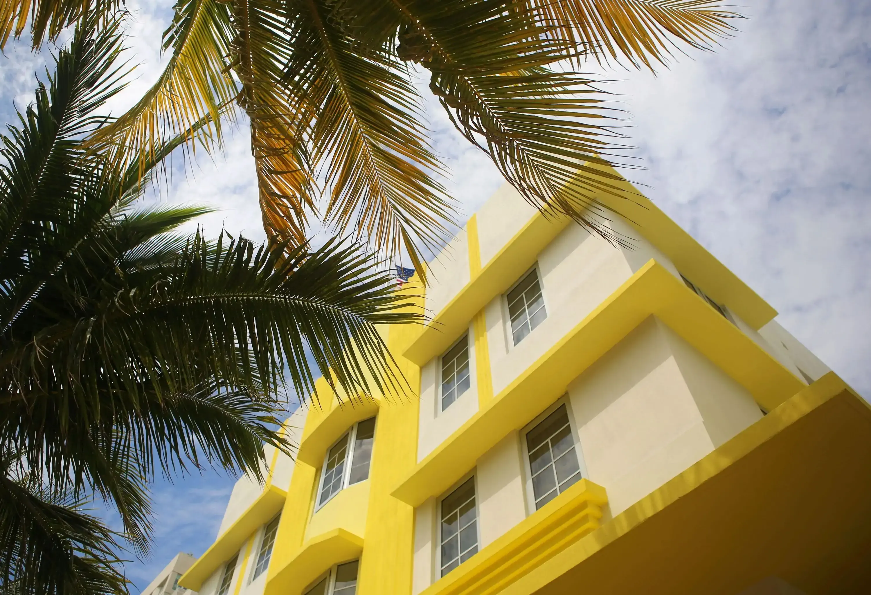 A white and yellow building and the fanning fronds of coconut trees against the sky.