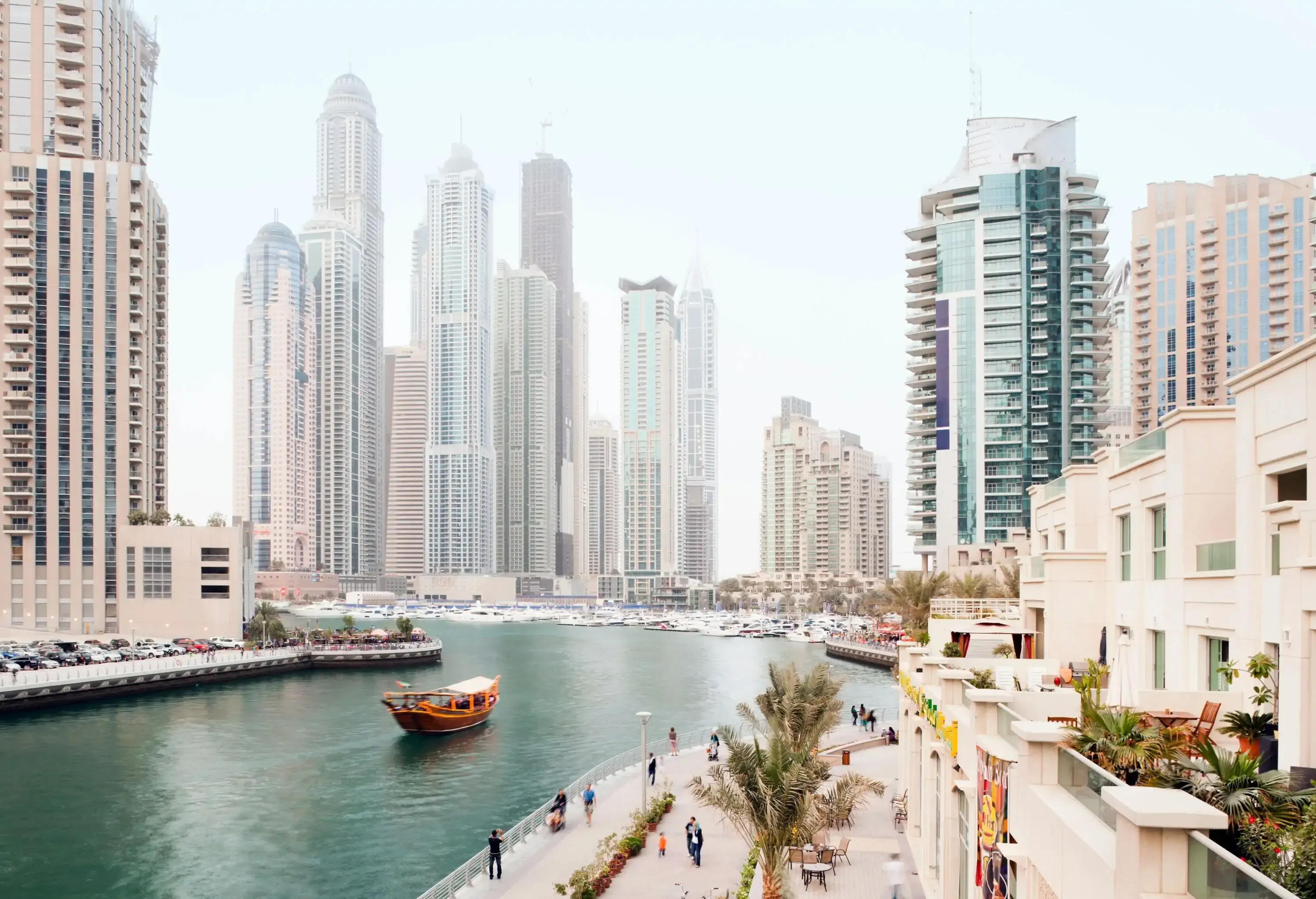 The affluent Dubai Marina skyline with canal-side promenades lined with restaurants and high-rise buildings.