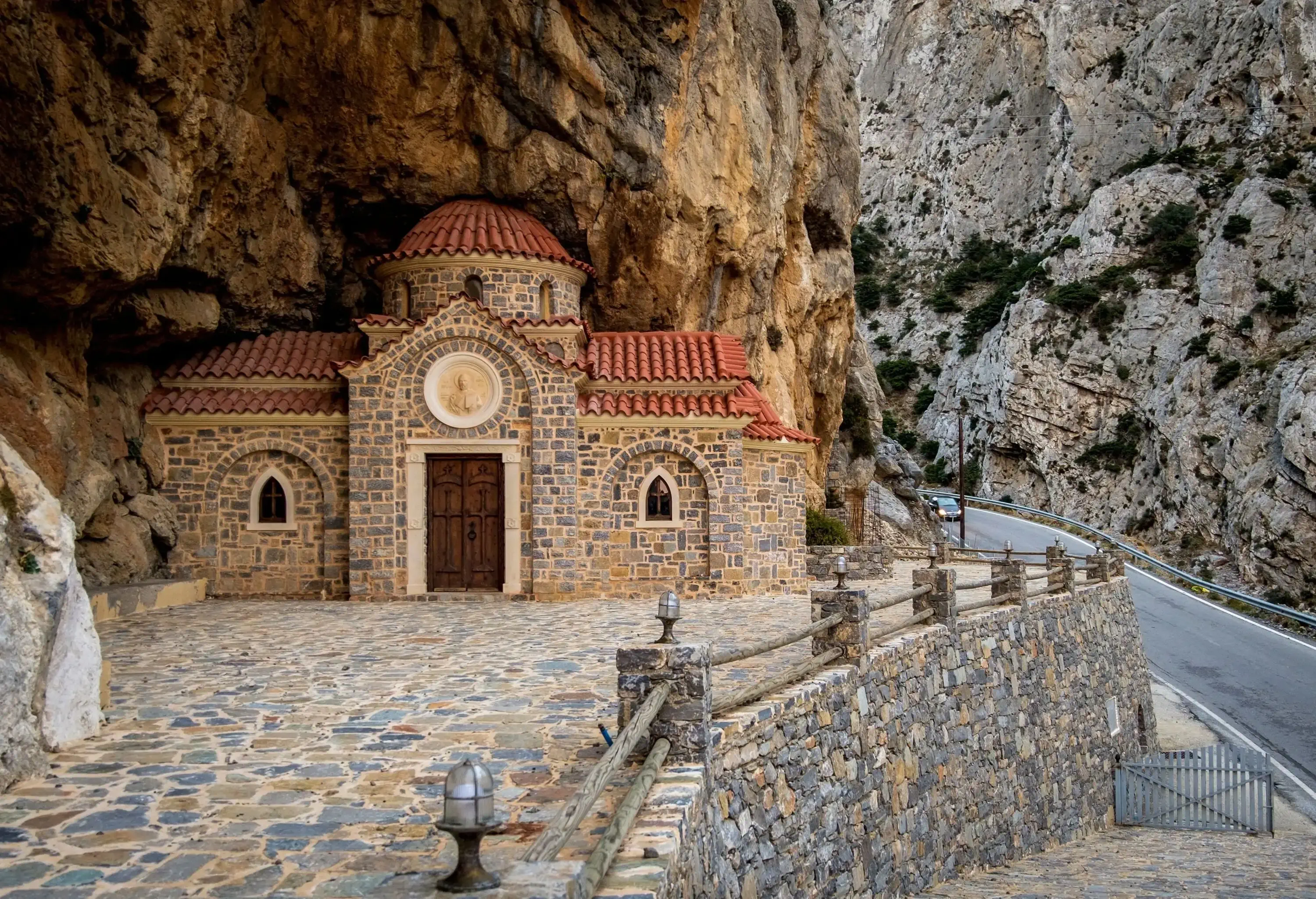 A stunning little church hidden in a rock cave along a road passes through narrow cliffs.