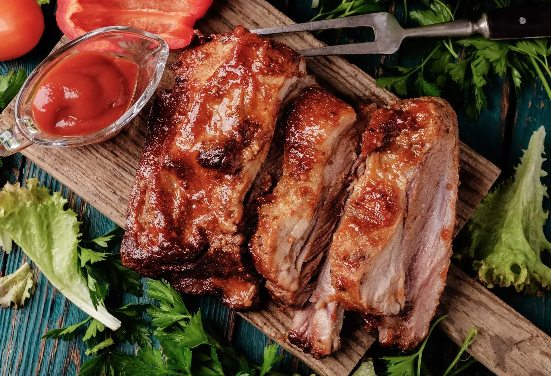 Delicious barbecued ribs seasoned with a spicy basting sauce and served with chopped fresh vegetables on an old rustic wooden chopping board in a country kitchen. Top view.