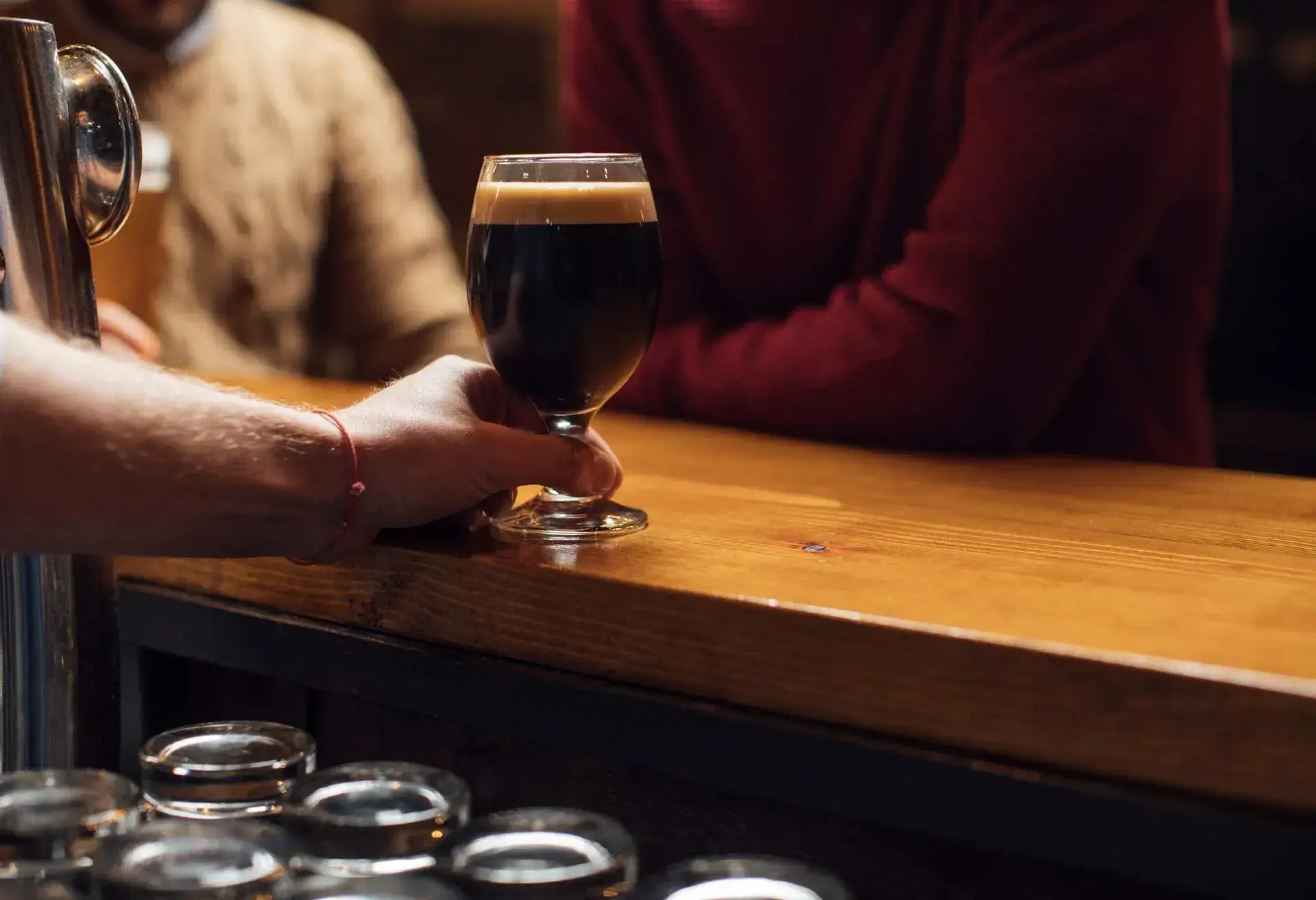 A hand serves a glass of drink to the customers at the bar.