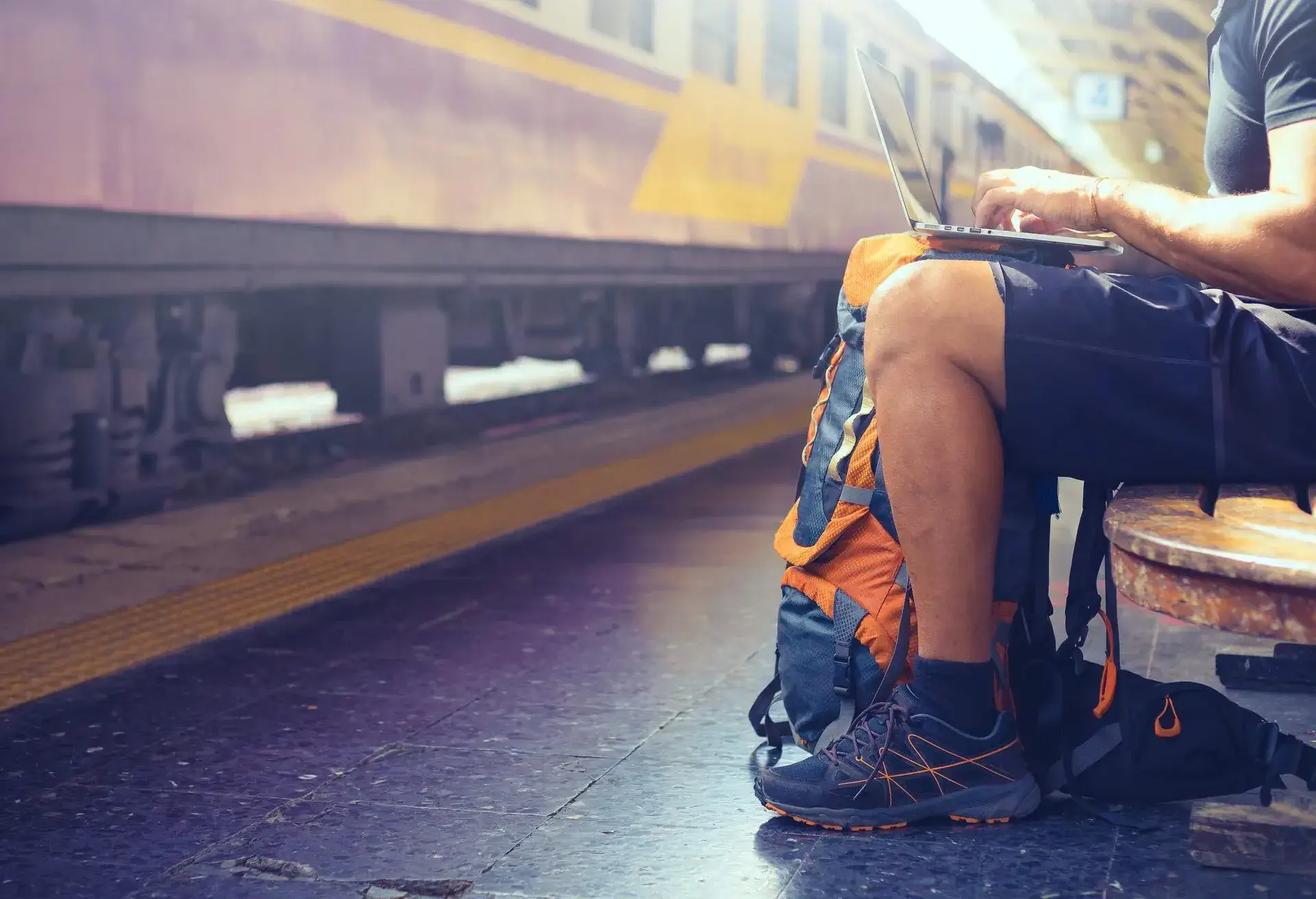 Digital nomad backpacker working on computer while waiting for train .