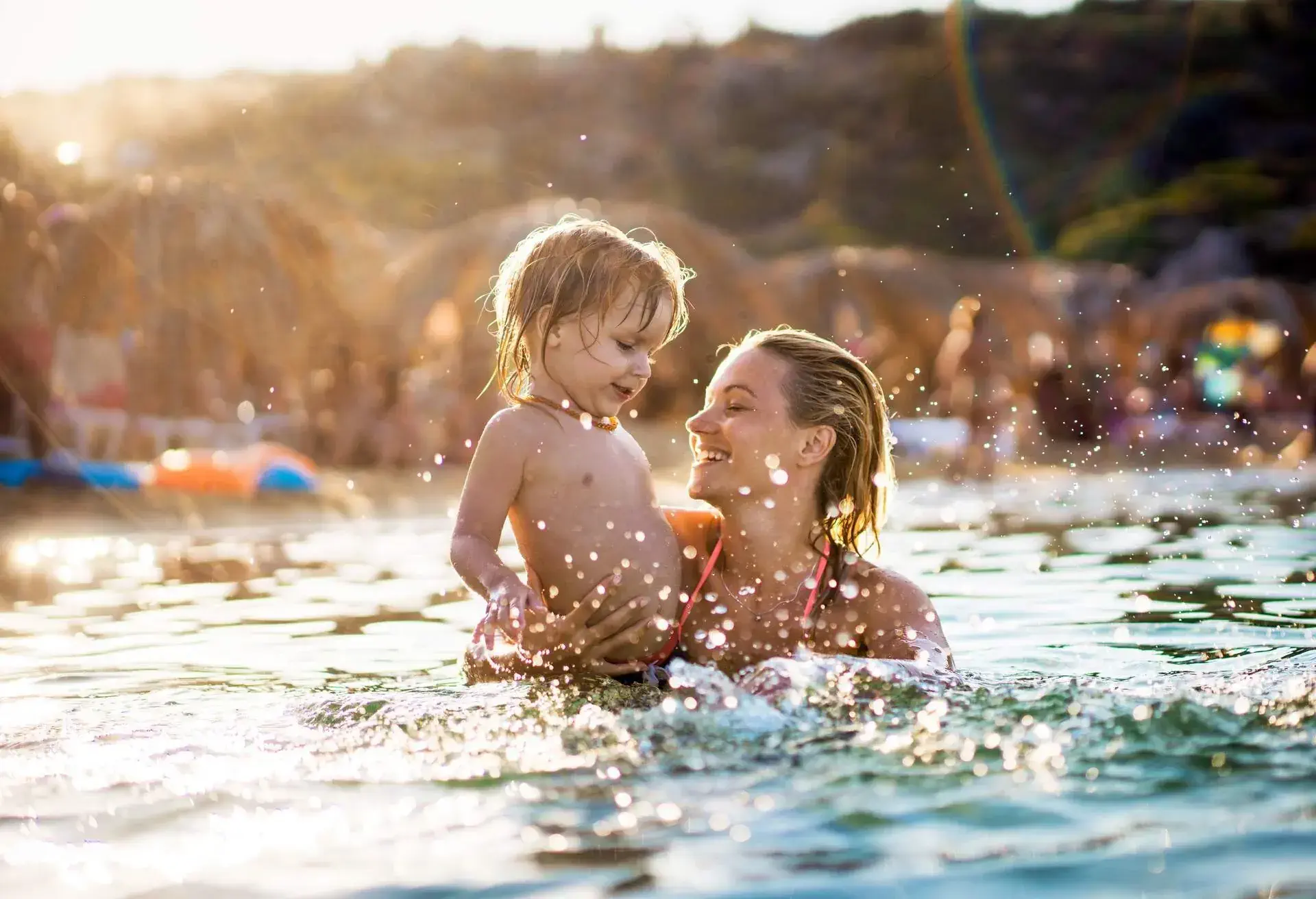 Young playful mother enjoying with her small boy while swimming in the sea.