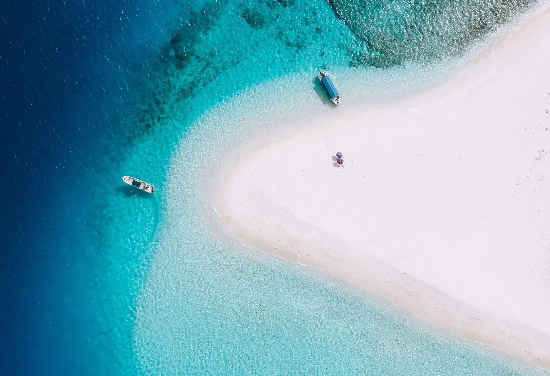 Aerial view of coral cay with clear blue tropical water, boats and parasols, Kerama Islands National Park, Okinawa, Japan