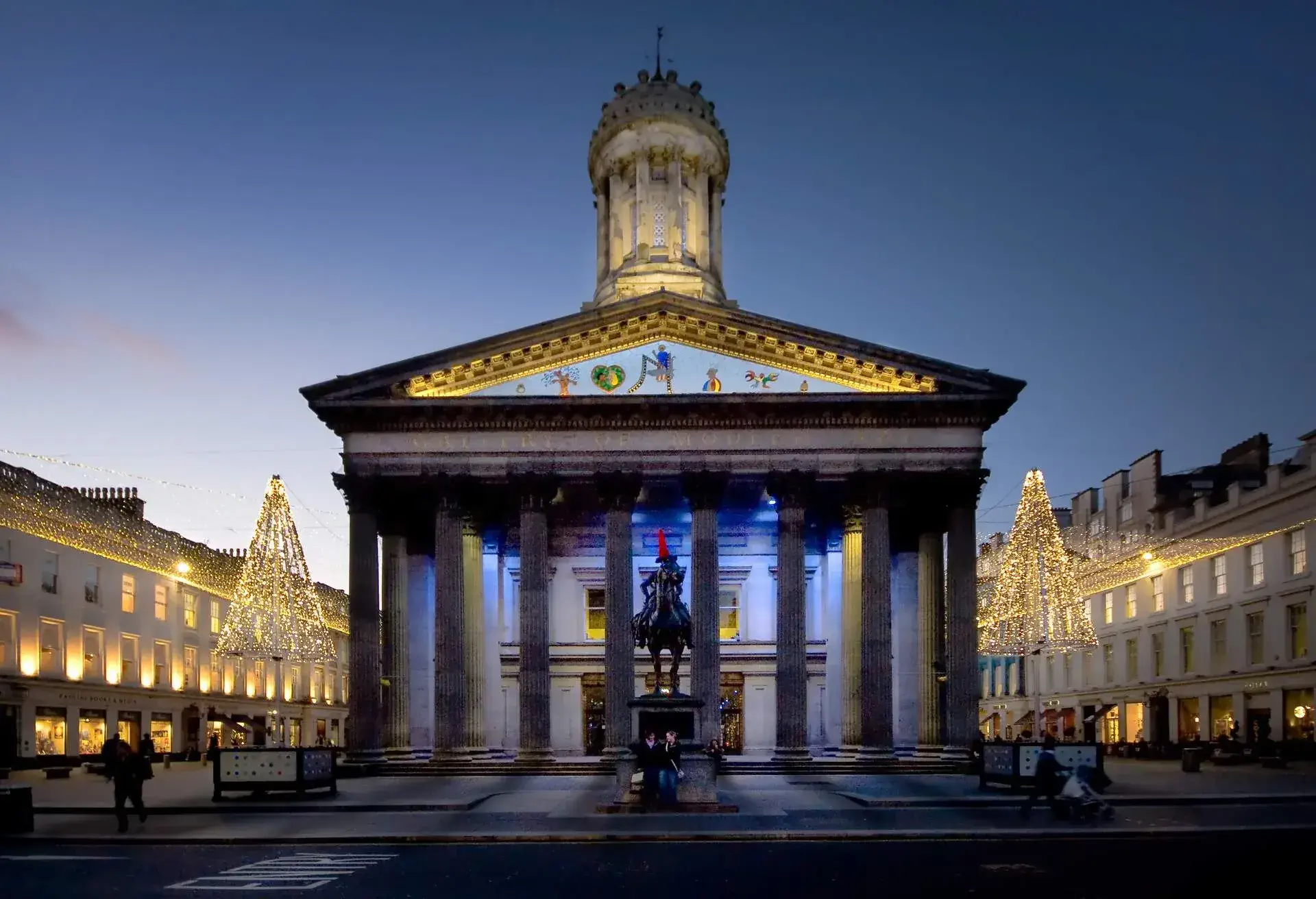 Brightly lit modern art gallery building with a statue of a man on horseback in front.