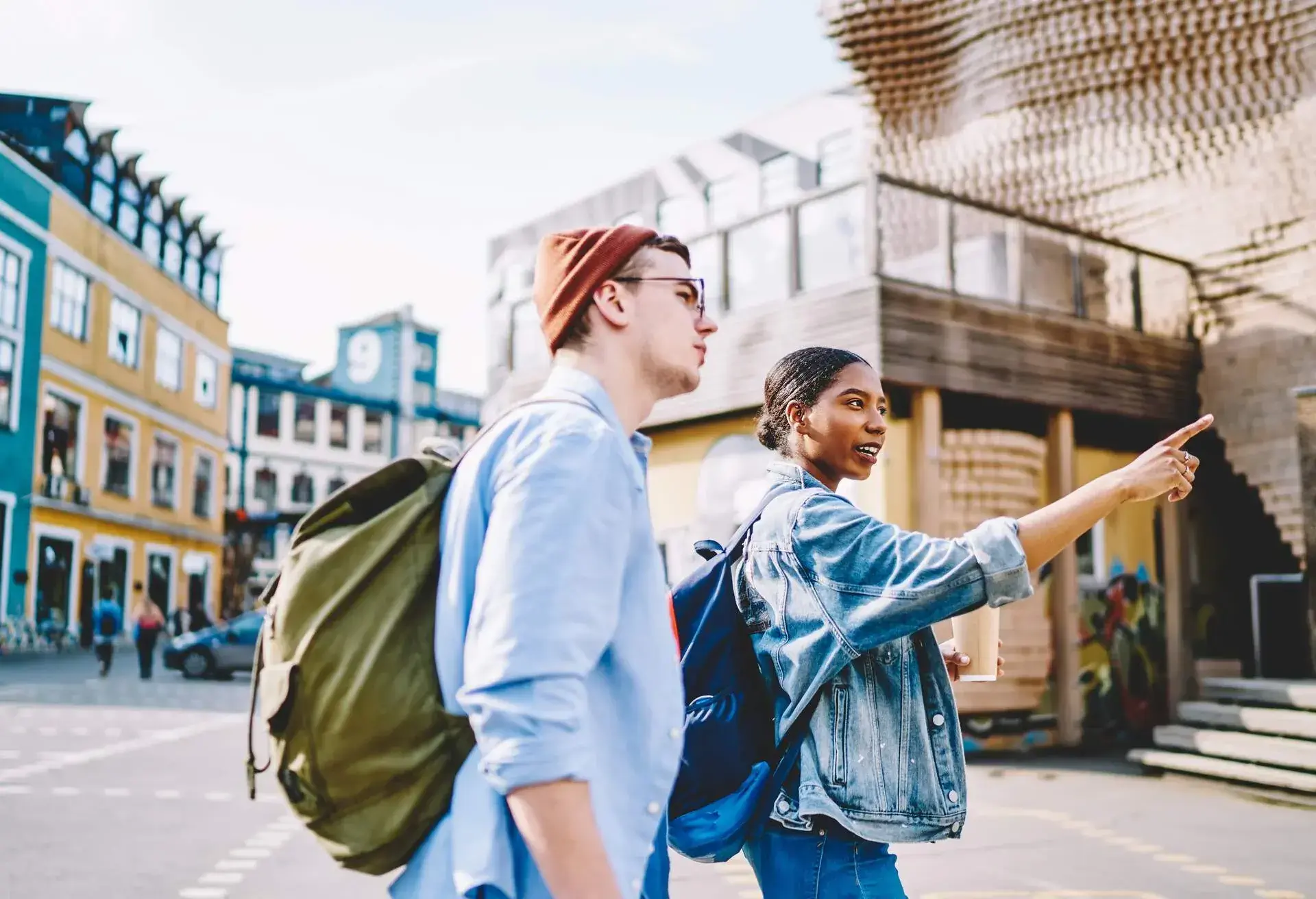 Multicultural male and female backpackers discussing showplaces while exploring touristic city, diverse man and woman in casual clothing walking and communicating during travel tour on vacations