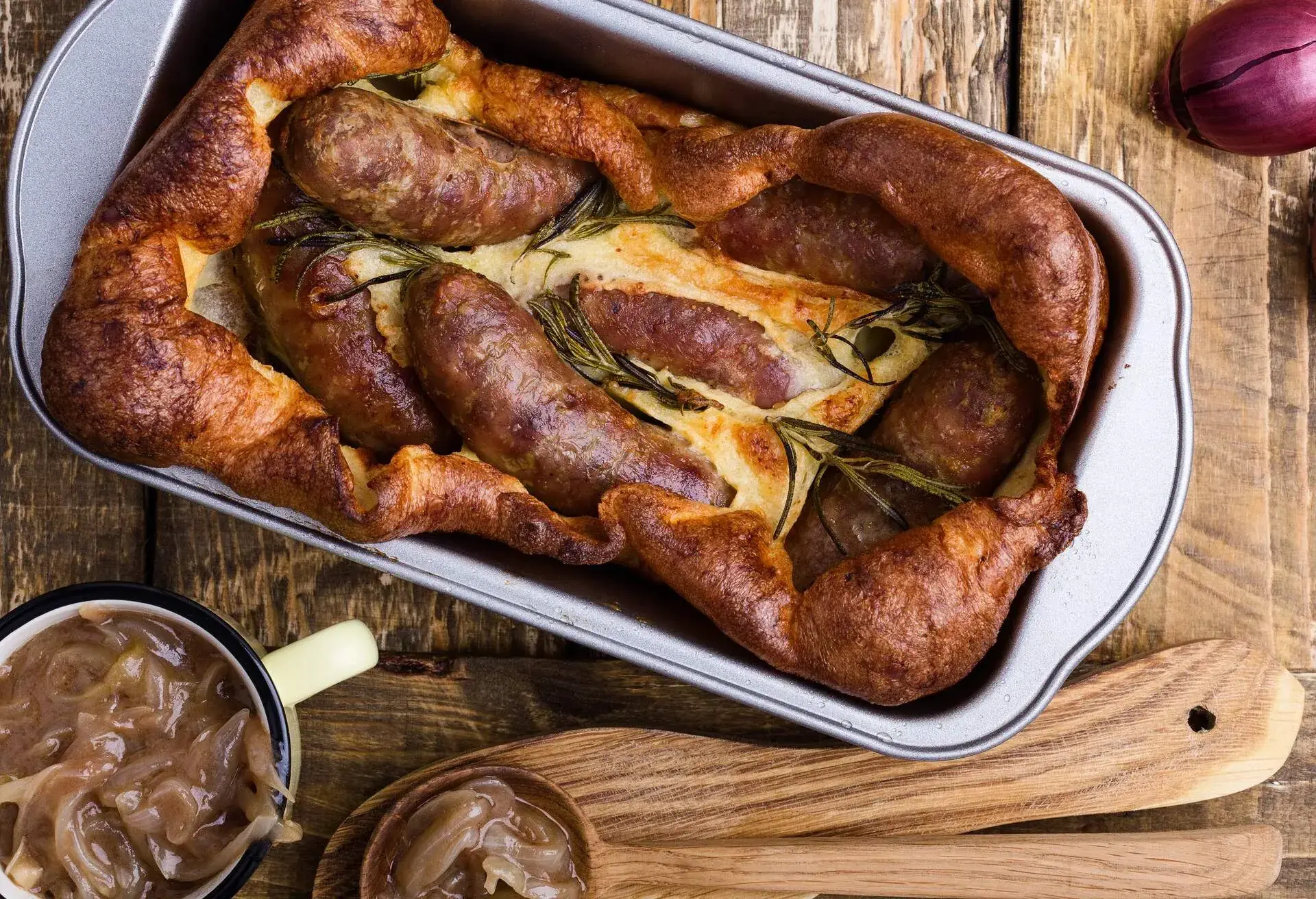 Baked sausages in Yorkshire pudding batter, toad in the hole with onion gravy on rustic wooden table viewed from above