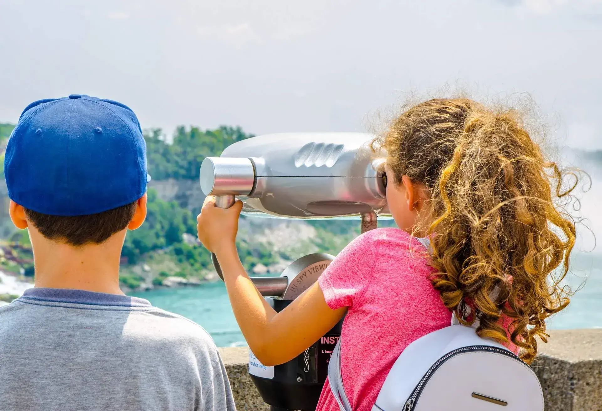 Girl and boy looking at Niagara falls through paying binoculars during summer day from Canadian side