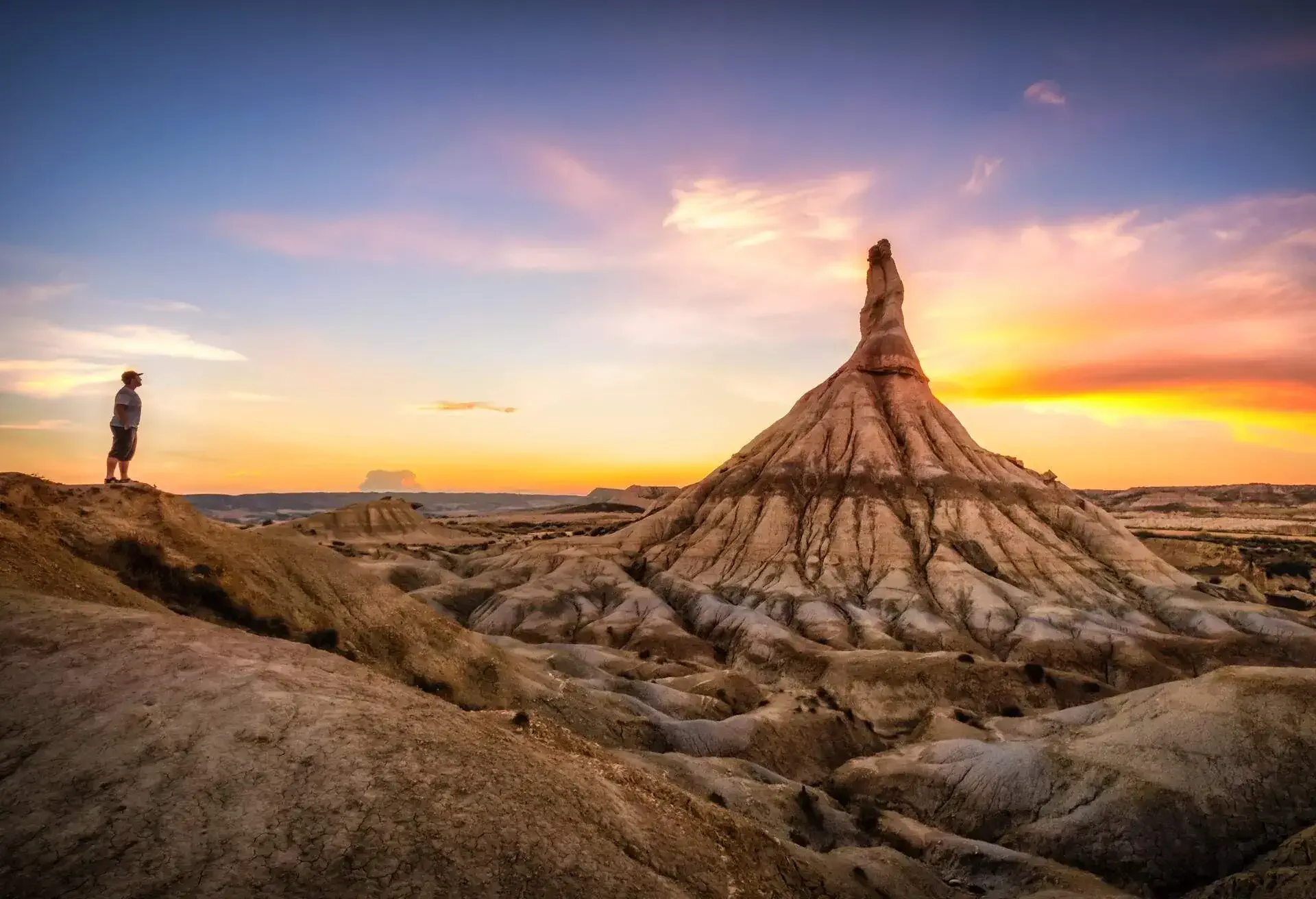 Man on top of desert mountain in Las Bardenas Reales at sunset, in front of Castildetierra Hoodoo. Navarra, Spain
