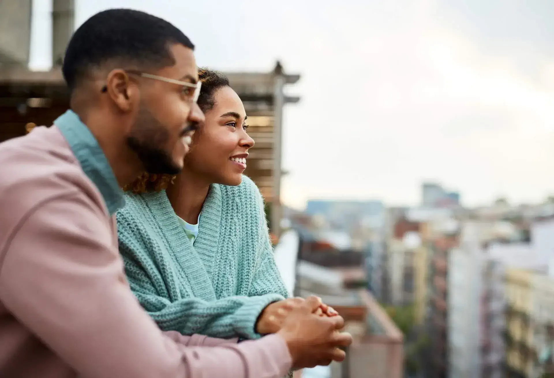 Happy young couple looking away while holding hands at rooftop. Smiling woman is spending leisure time with boyfriend. They are enjoying at building terrace.