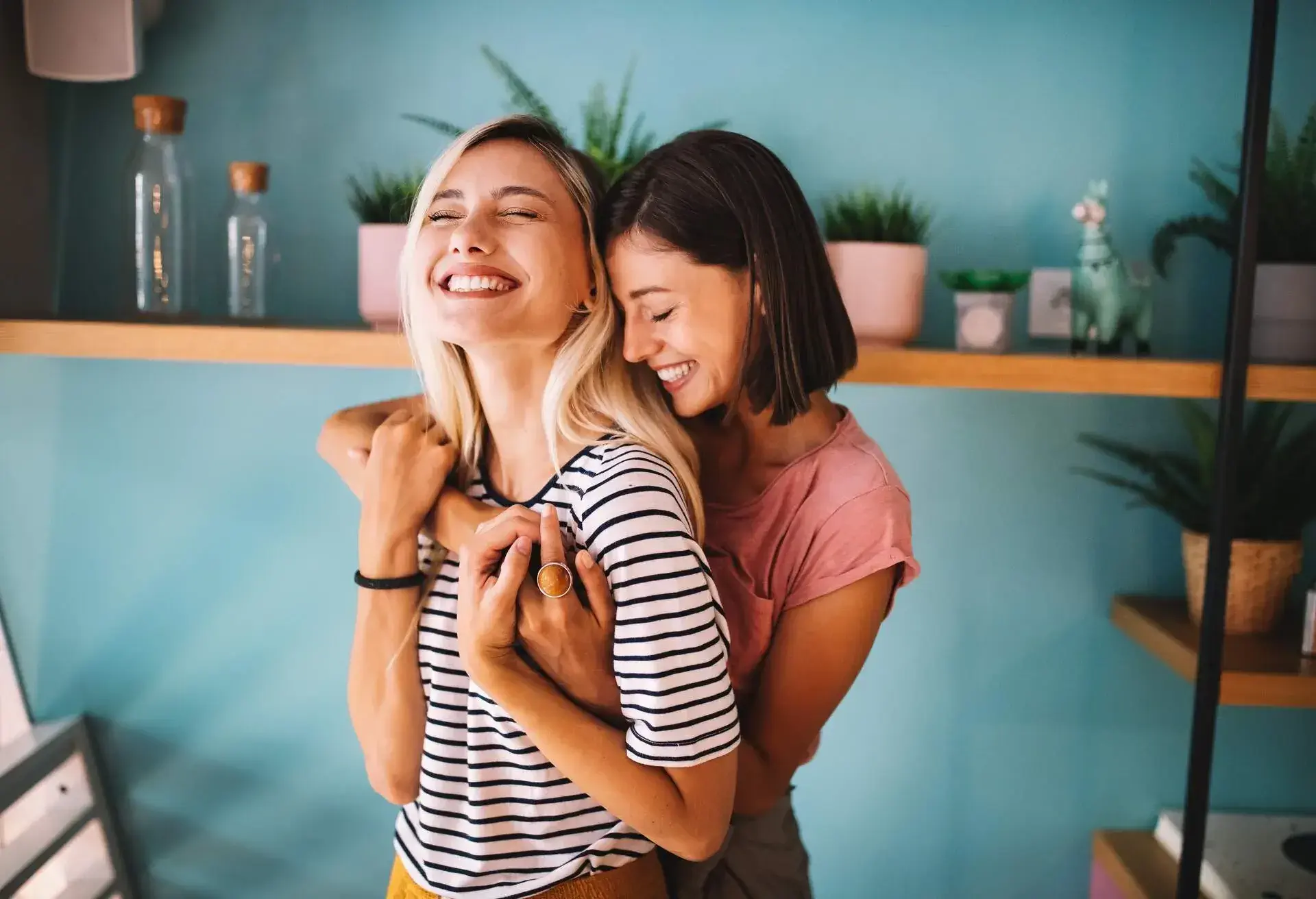A woman gives her partner a back hug while smiling with their eyes closed.