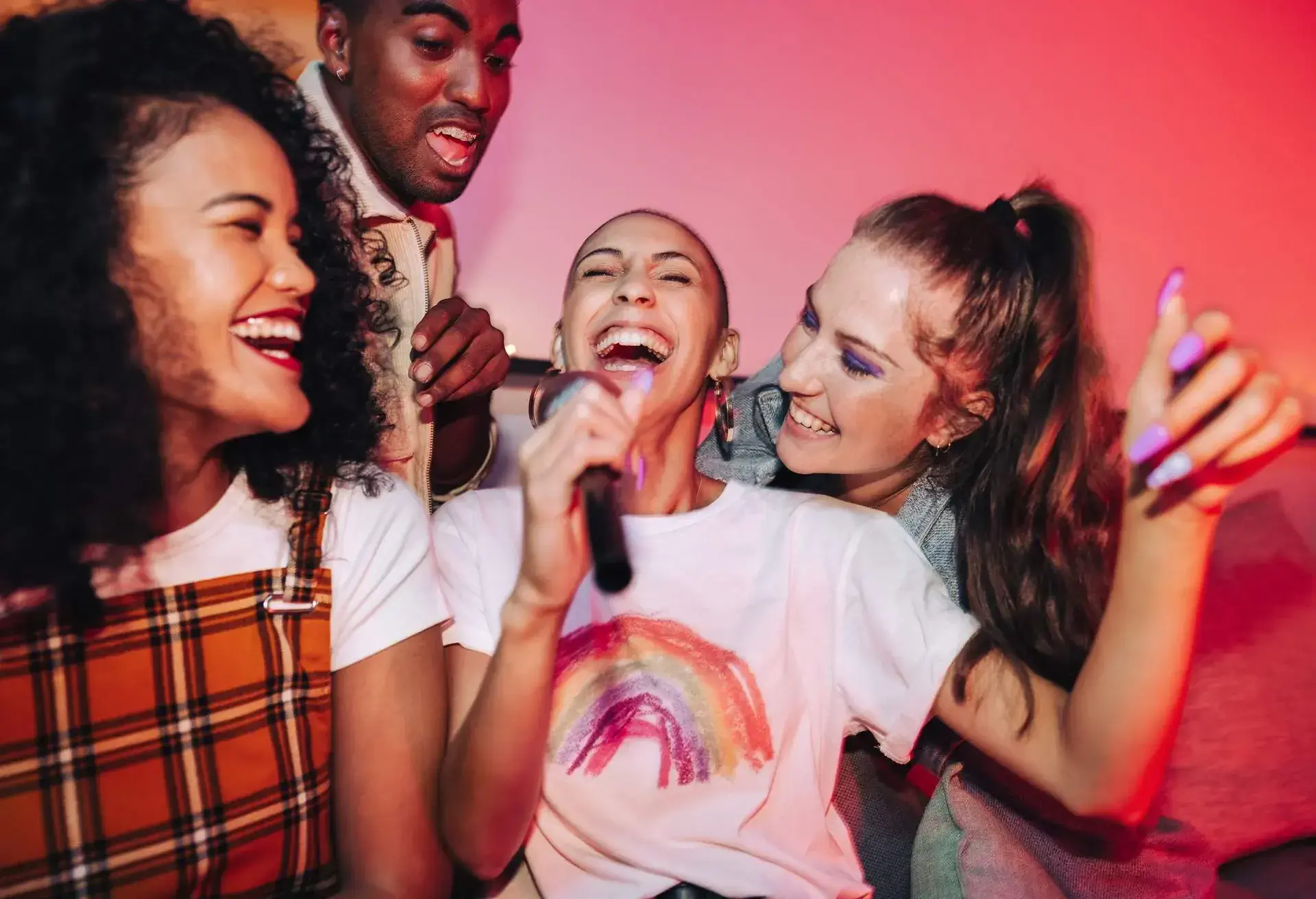 Joyful friends singing their favourite song during karaoke night. Happy young friends laughing joyfully at a house party. Group of multicultural friends having a good time on the weekend.
