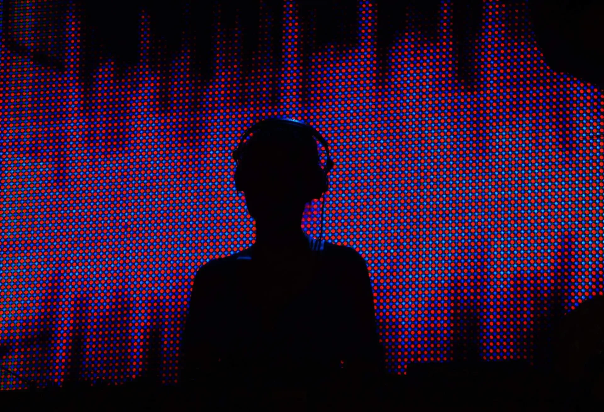 A DJ's silhouette against a neon background in a nightclub.