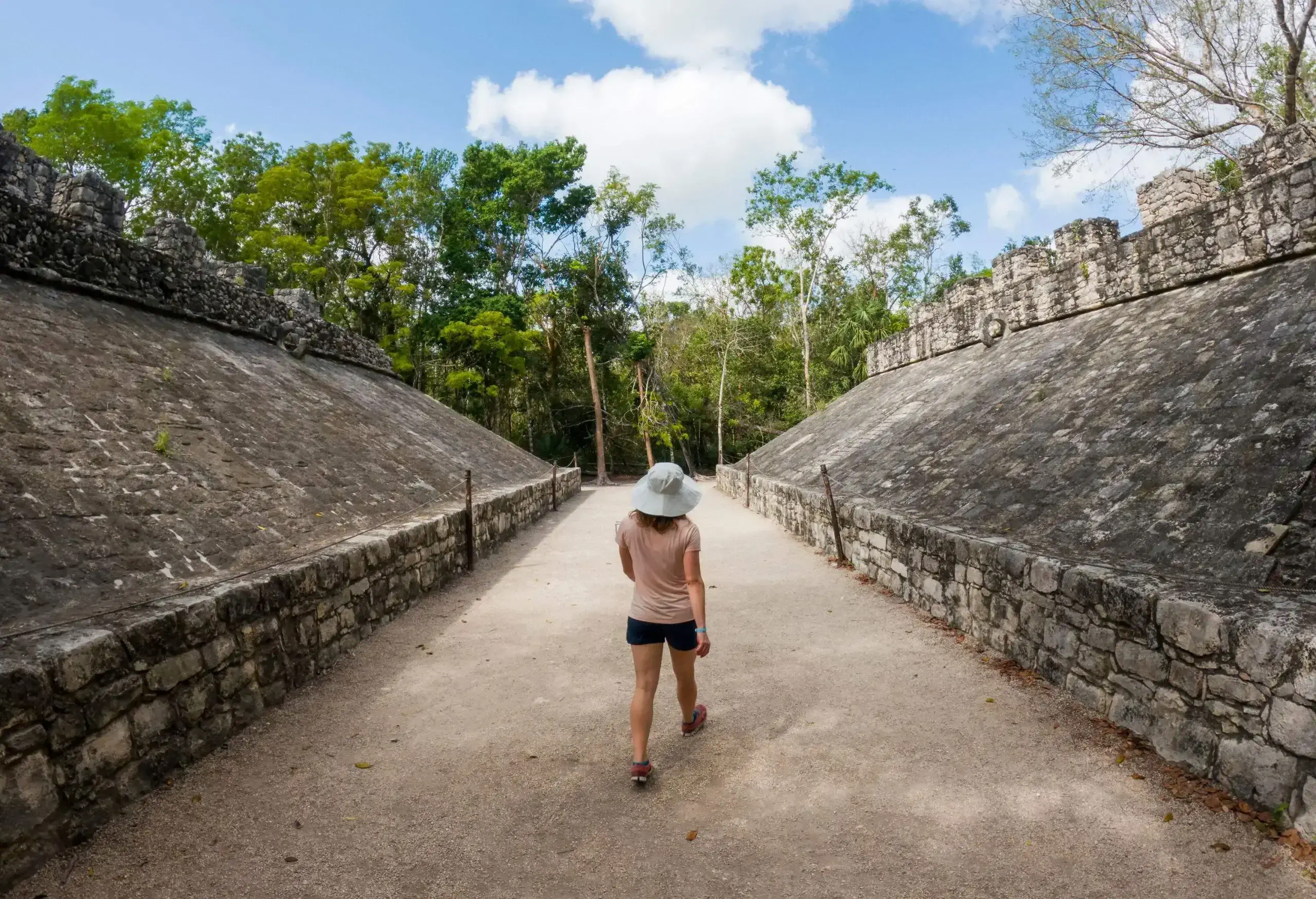 Back view of a young girl walking between the rock ruins surrounded by trees in a Mayan archaeological area.