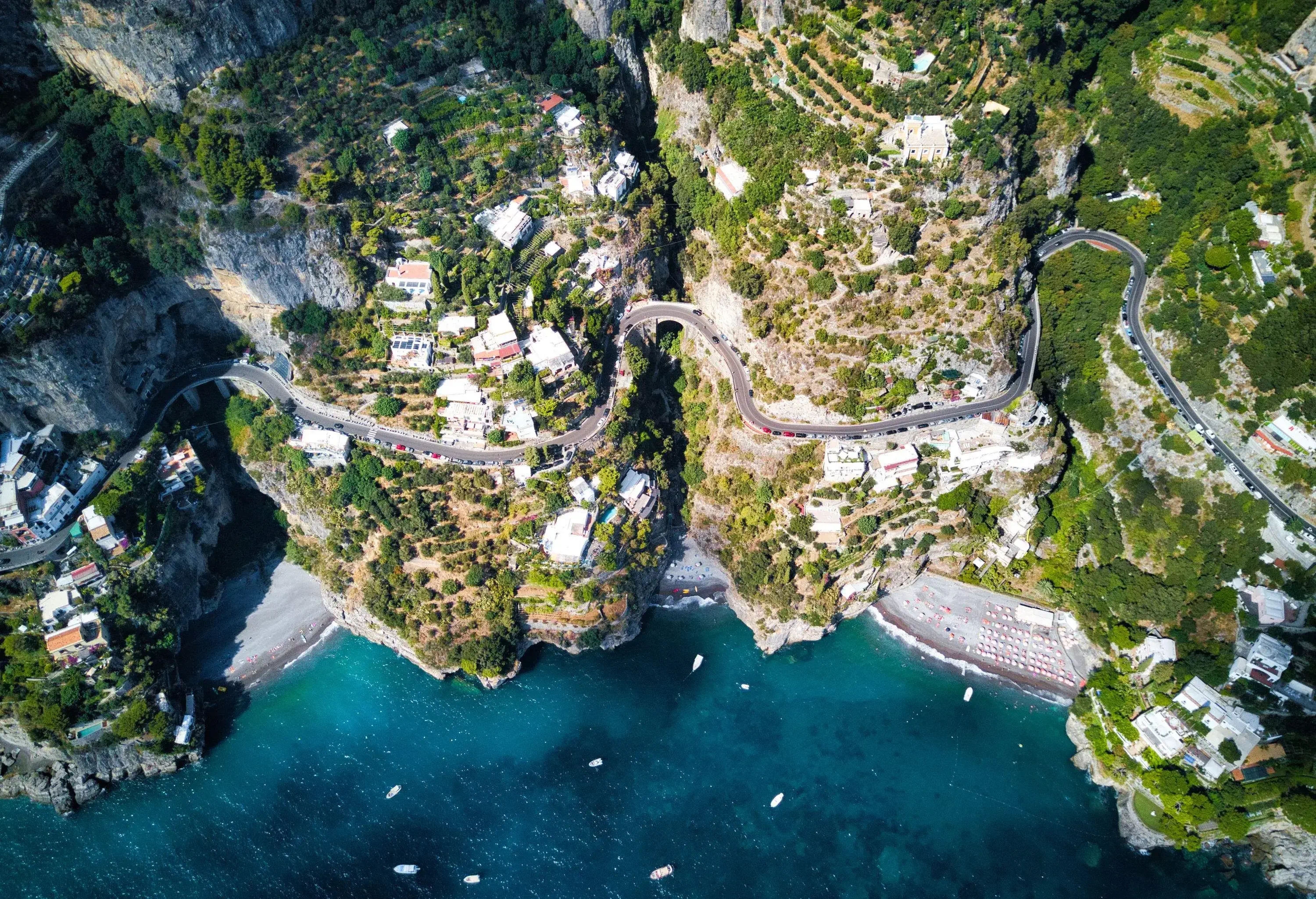 A winding road across a hillside coastal town with terraced buildings and lush trees.