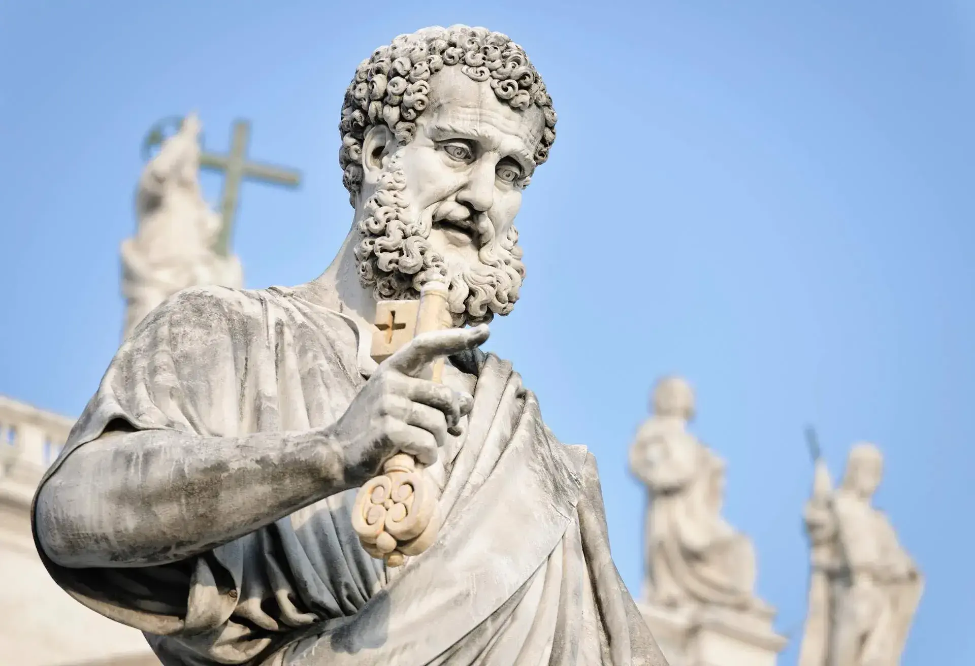 St. Peter's statue clutching a key, with other sculptures behind him, against a blue sky.