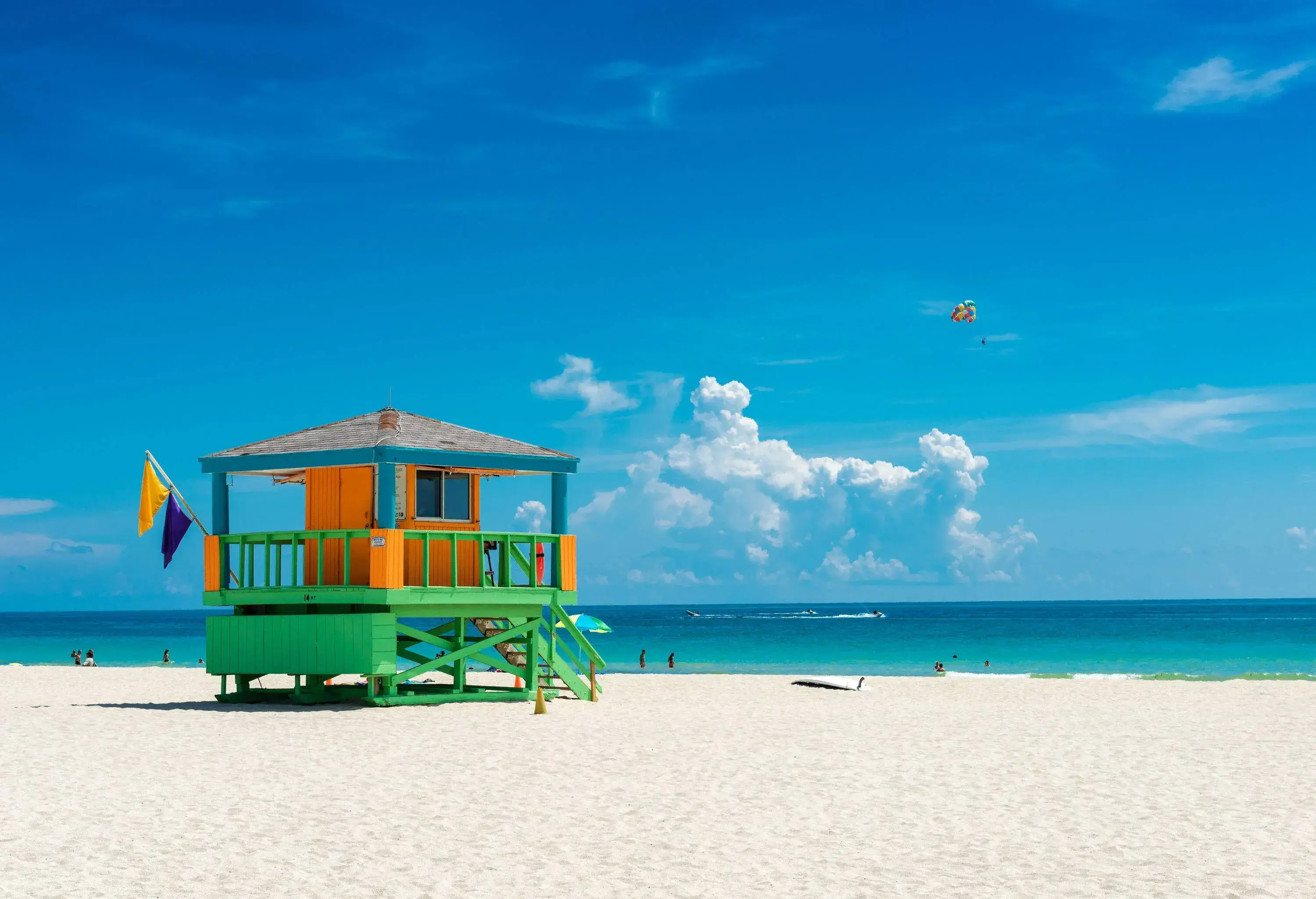 A colourful lifeguard tower with blue and yellow flags on a sandy beach.