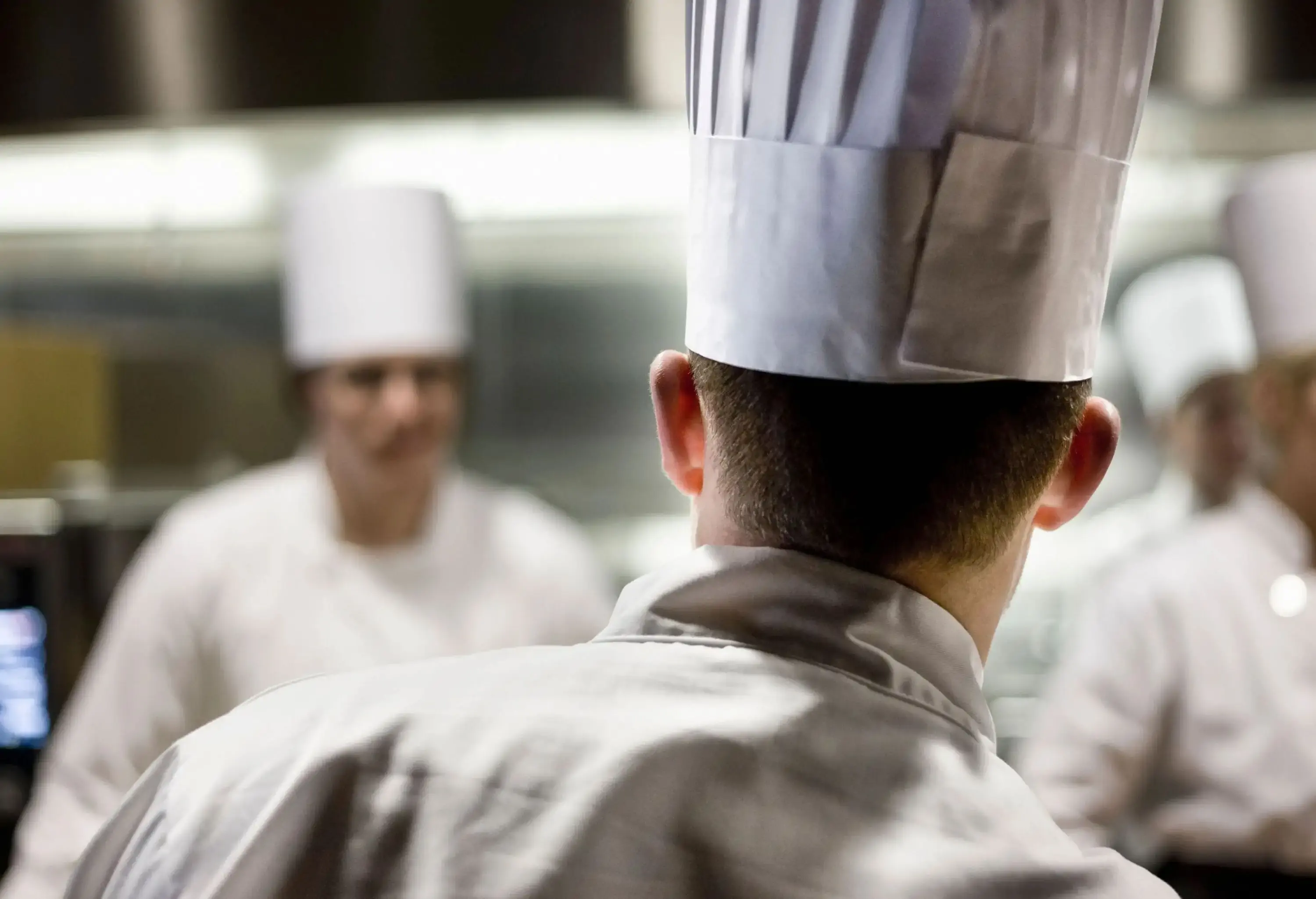 Group of chefs wearing toque hats inside a kitchen.