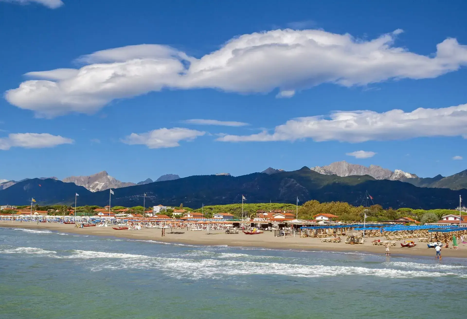 A beach with rows of sunbeds, umbrellas, and picnic tents.