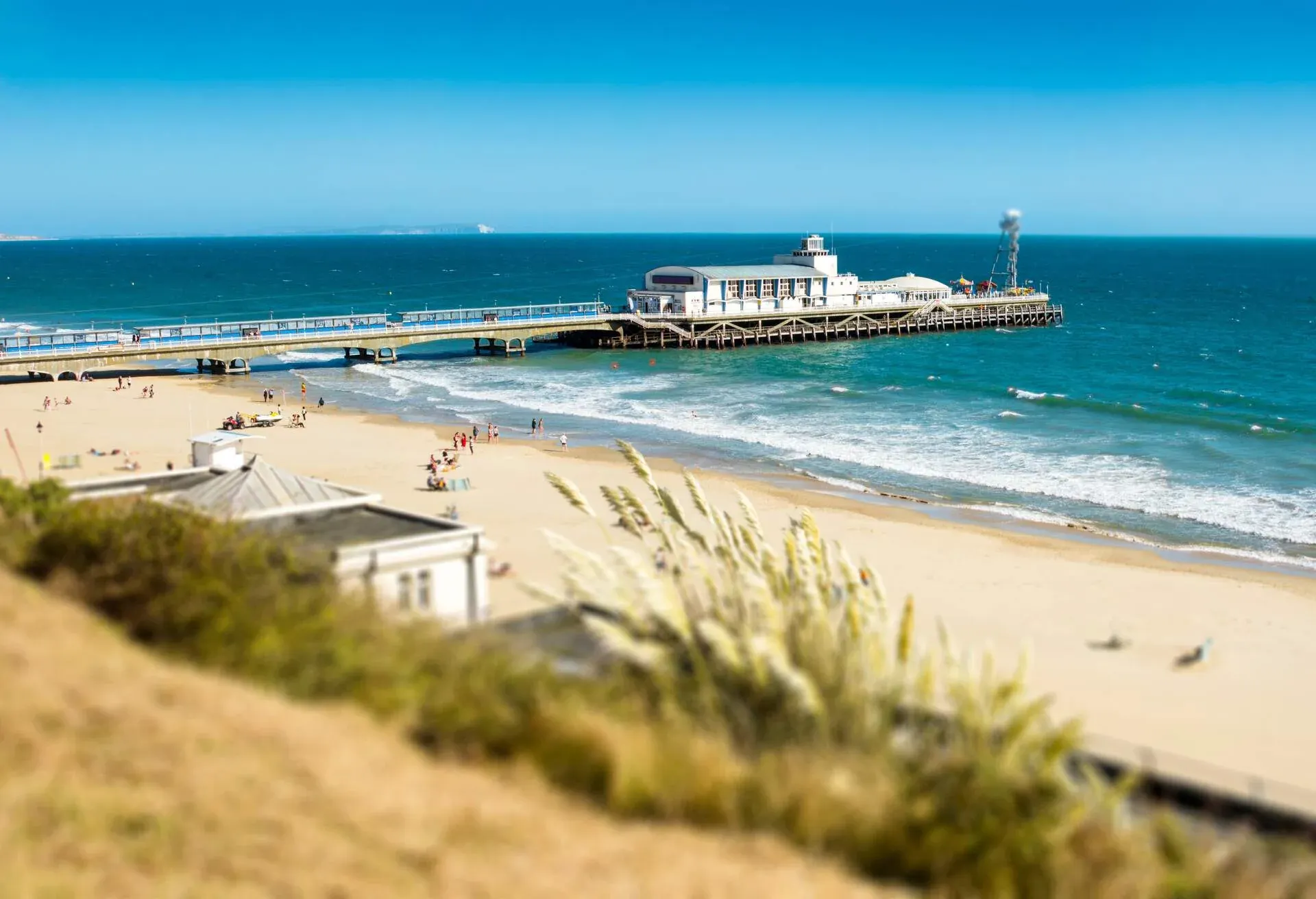 People out on the beach with a Victorian pier that plunges into the sea.