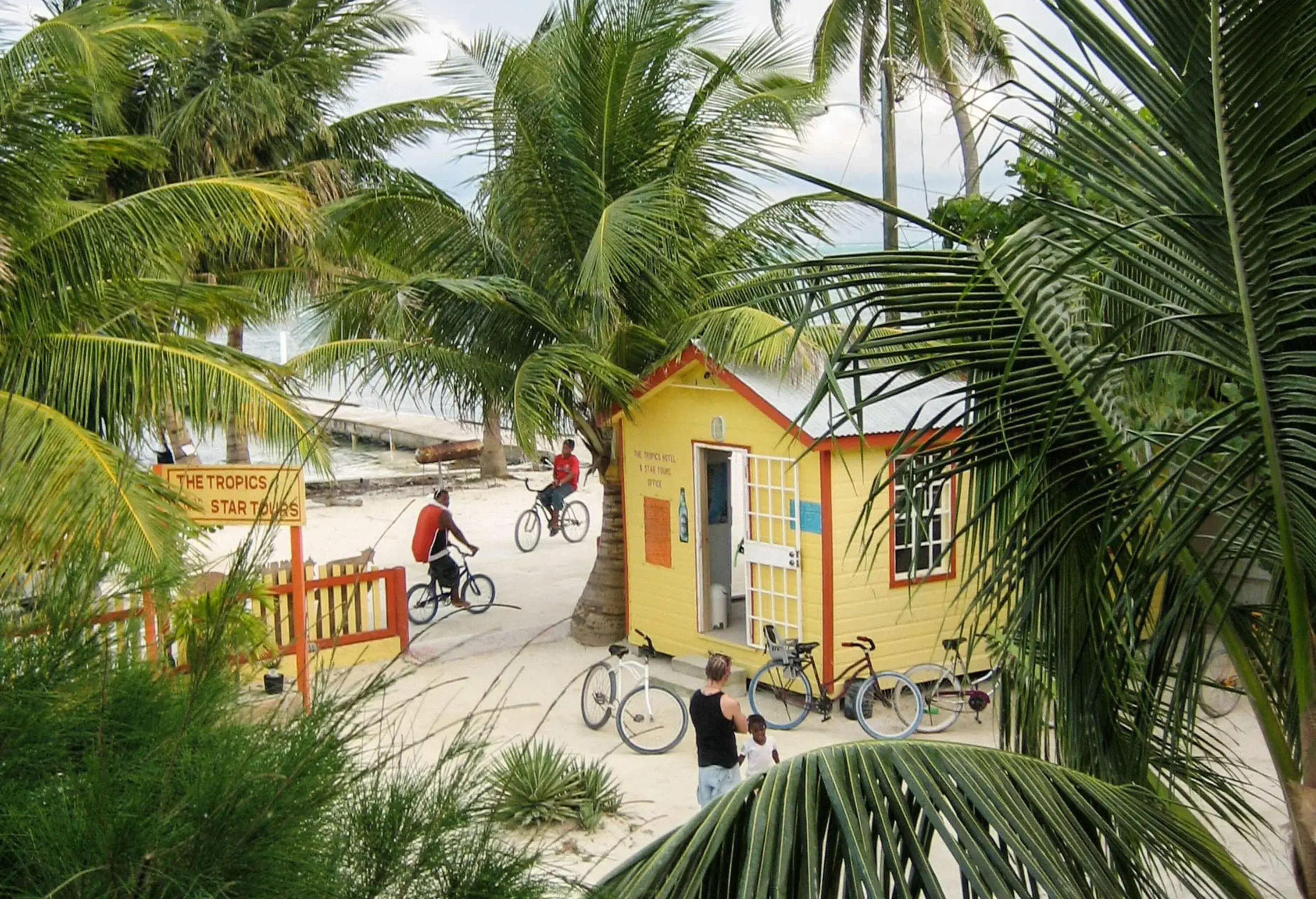 A tropical beach with bicycles propped up against a yellow beach hut surrounded by coconut trees.