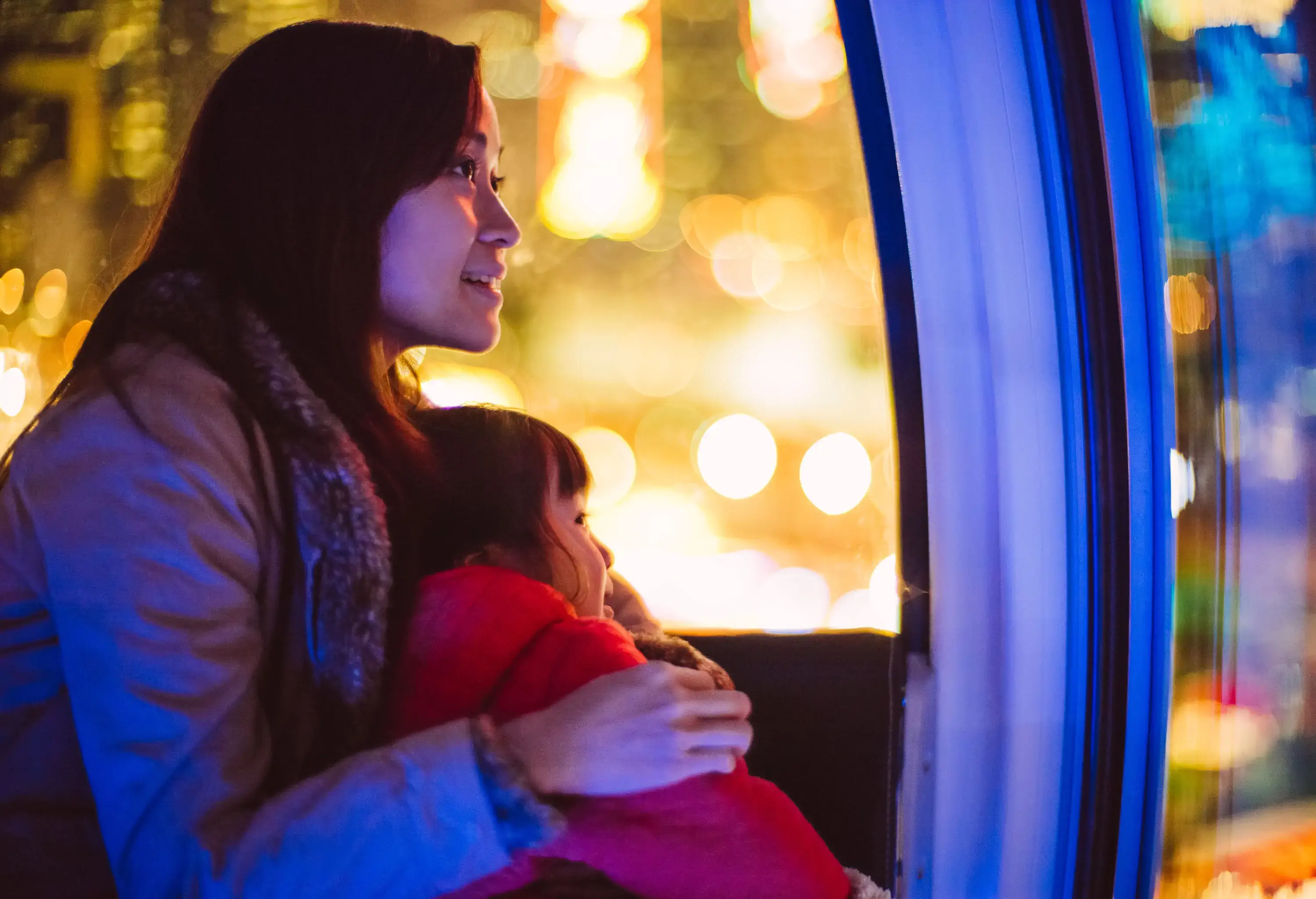 A woman and a small child riding a pod with bright lights shining through the glass windows.
