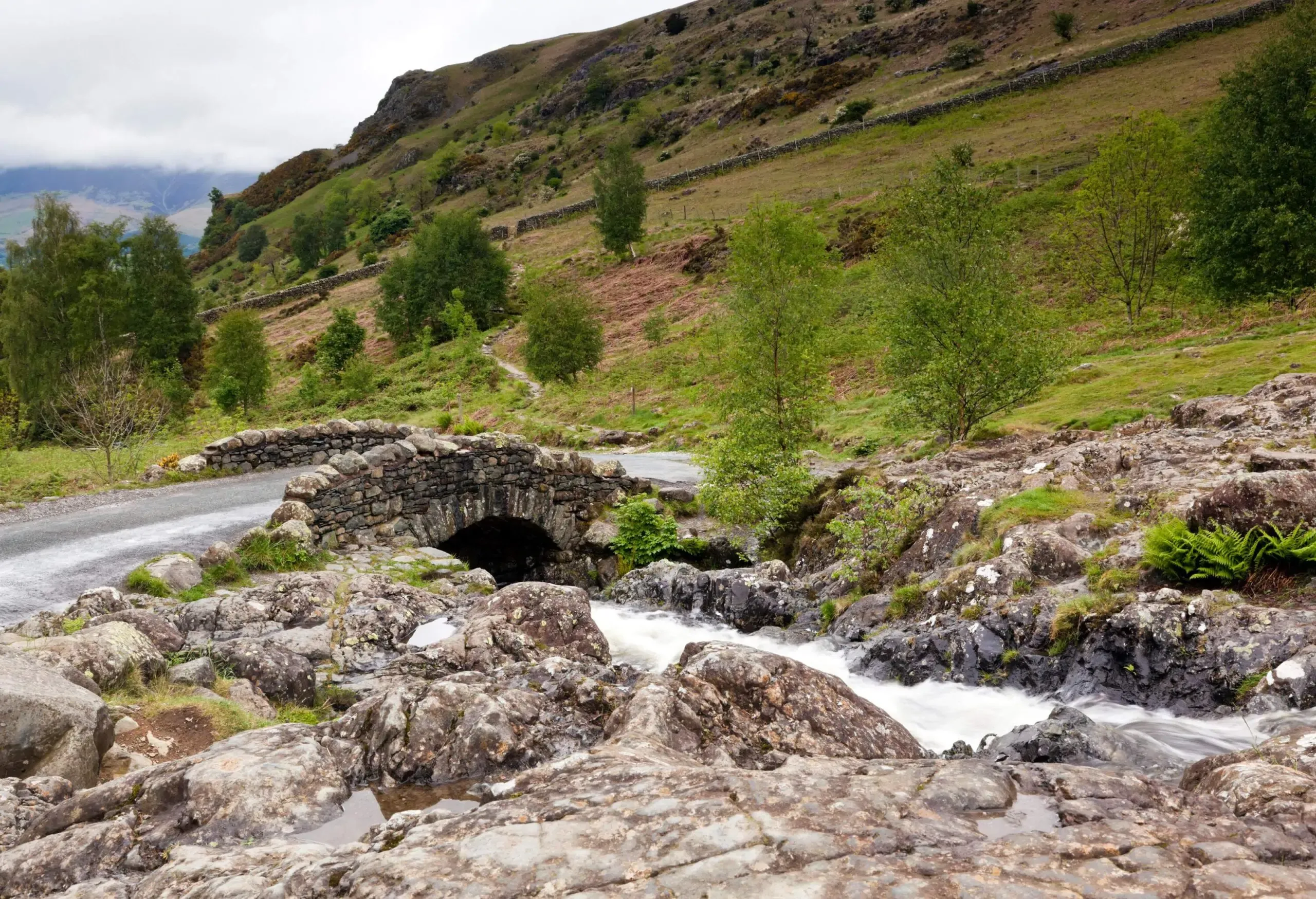 A stone bridge over a river with a rocky coast near a green valley.