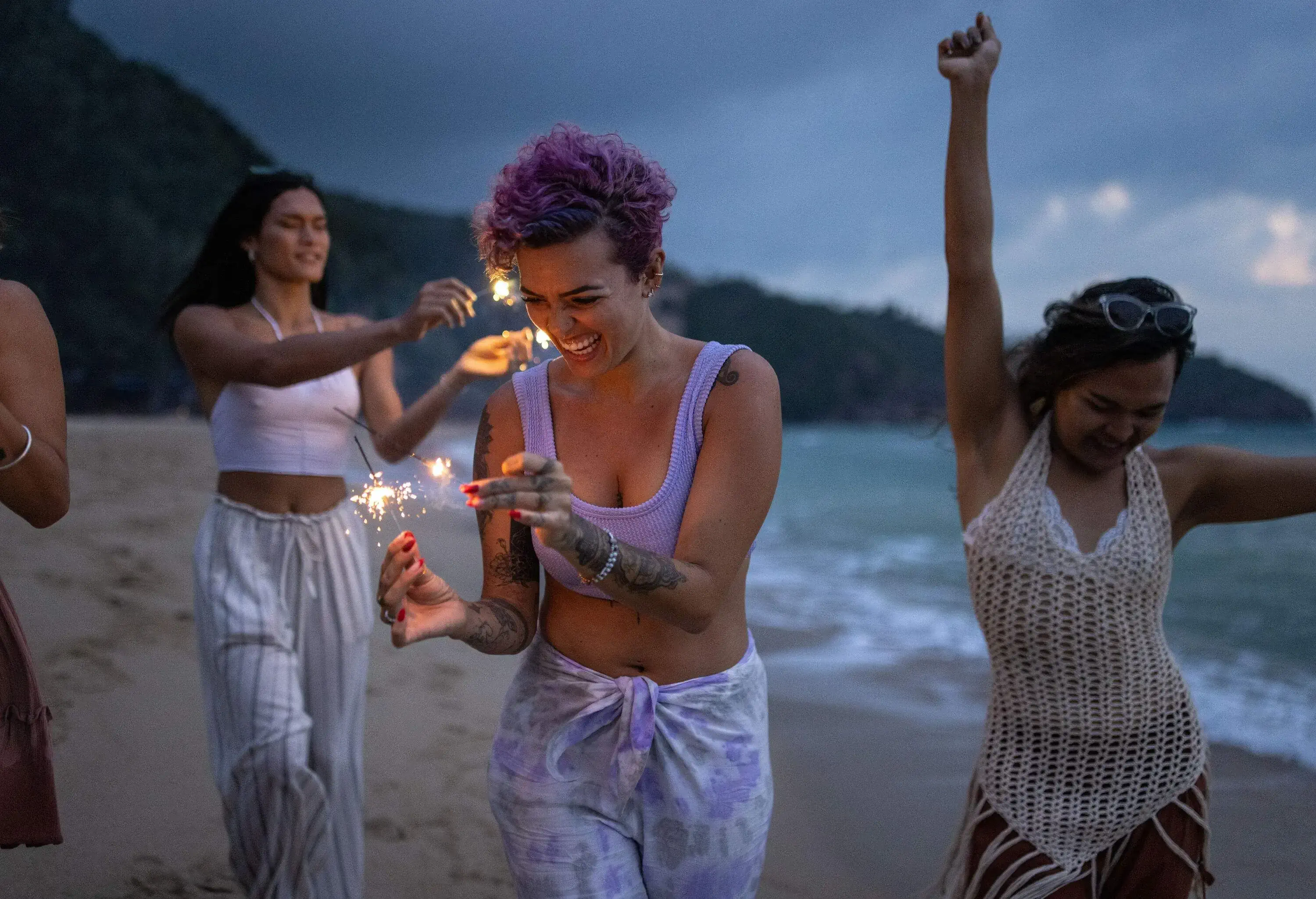 A group of friends lighting fireworks and dancing on the beach.