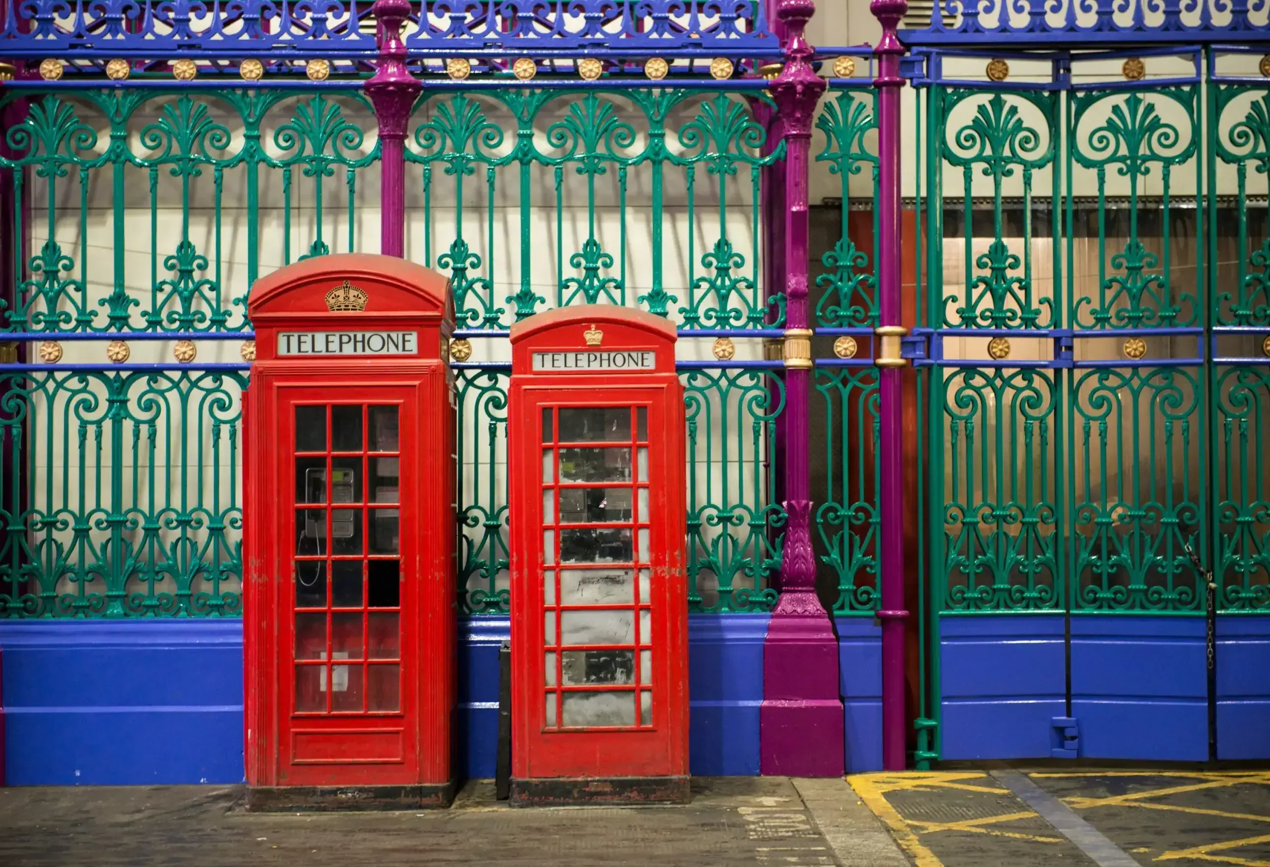 wo red phone booths by the road side adjacent to the green and purple iron fencing of Smithfield market. London UK.
