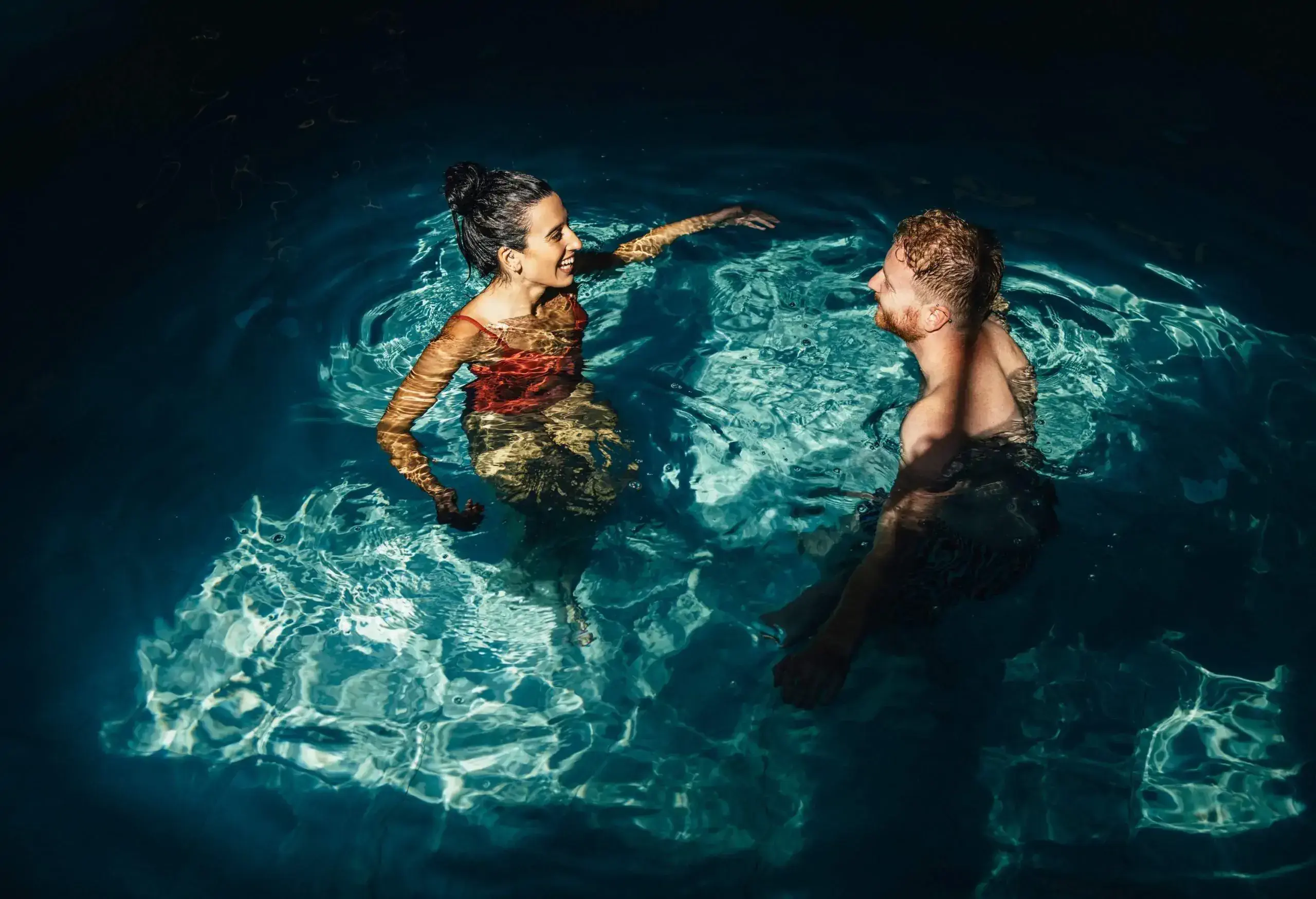 Smiling girlfriend and boyfriend in swimwear talking together in the swimming pool.