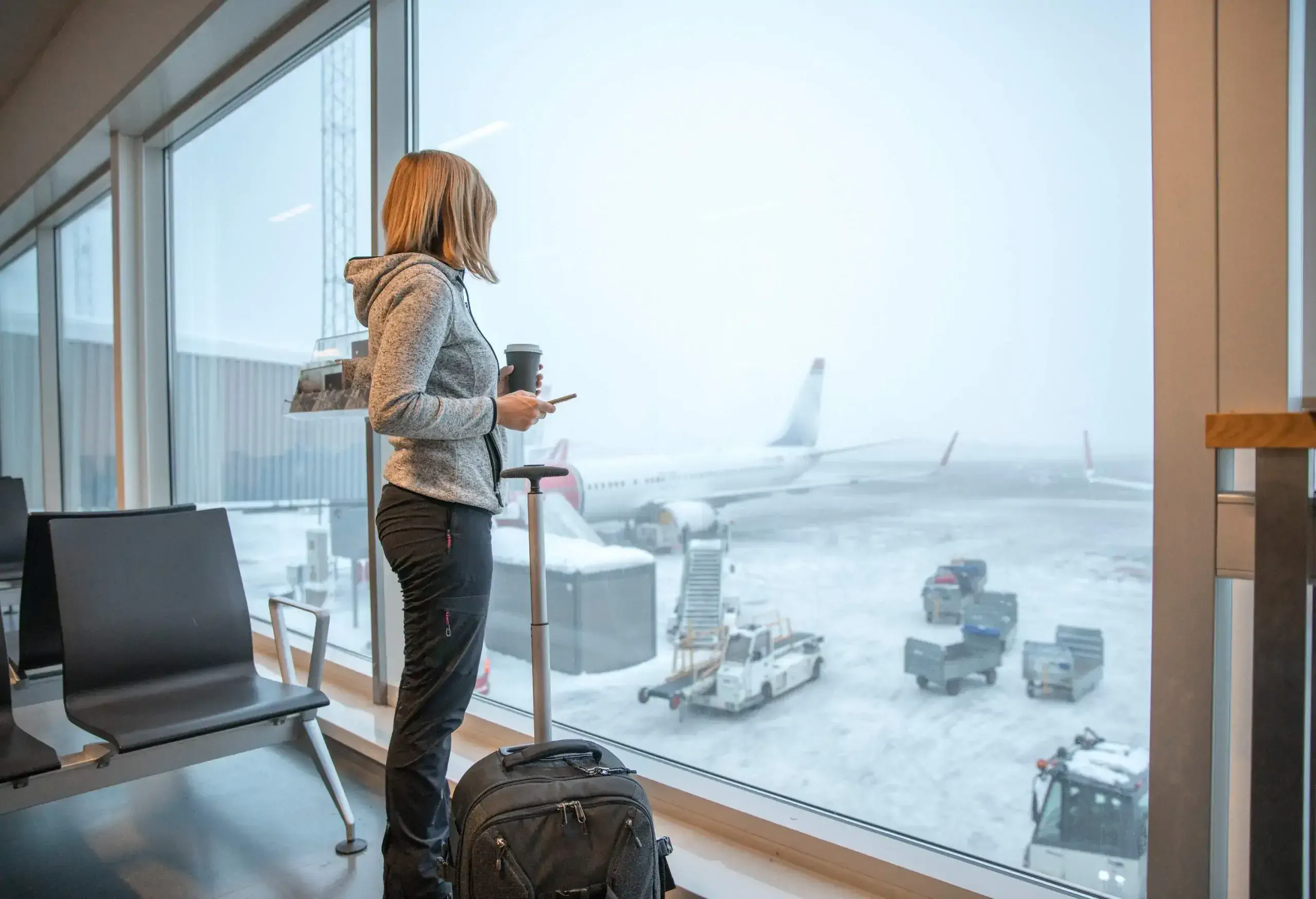 Woman standing close to window with luggage at airport.