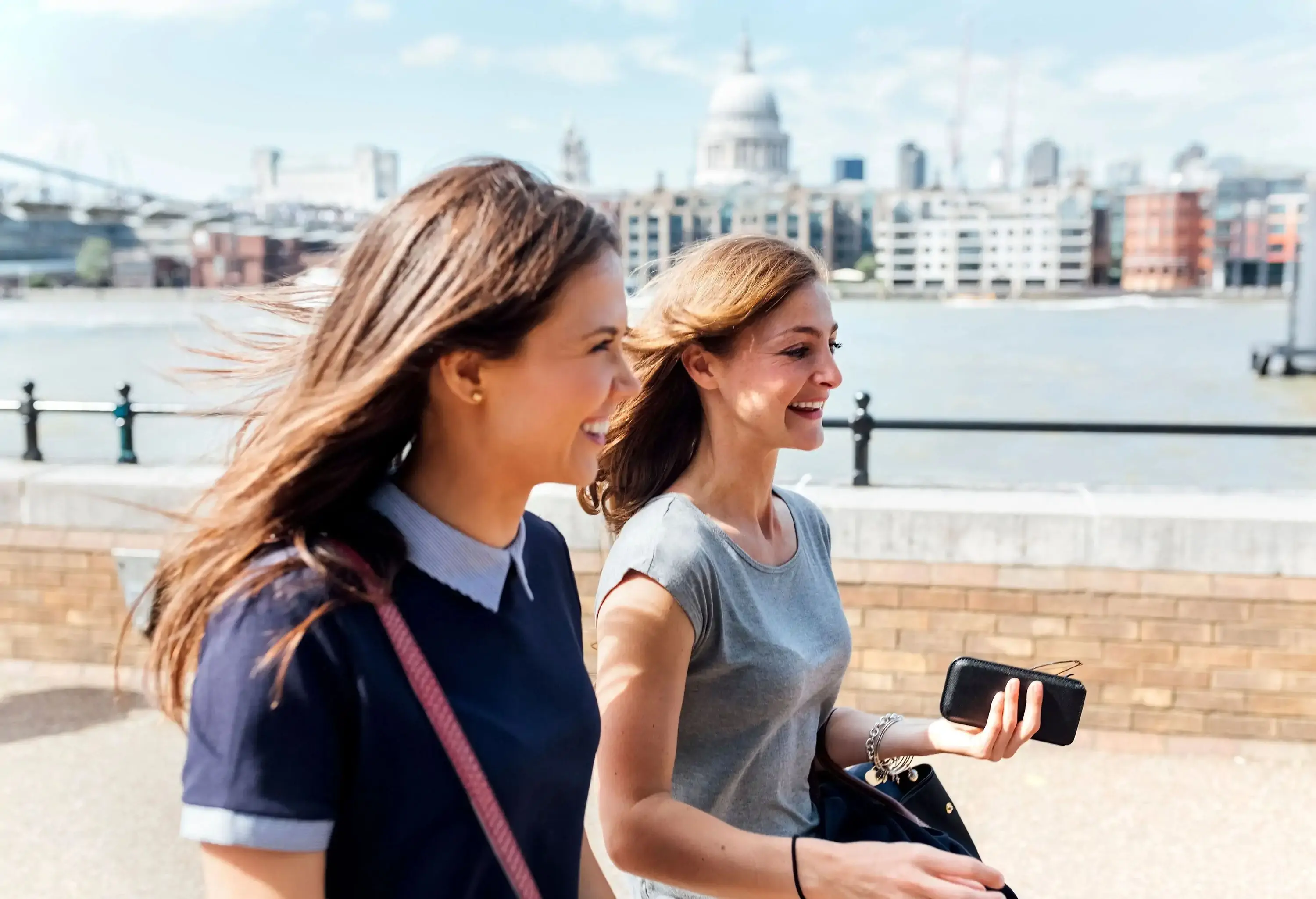 Two brunette women in casual clothes smile as they stroll together on a promenade.