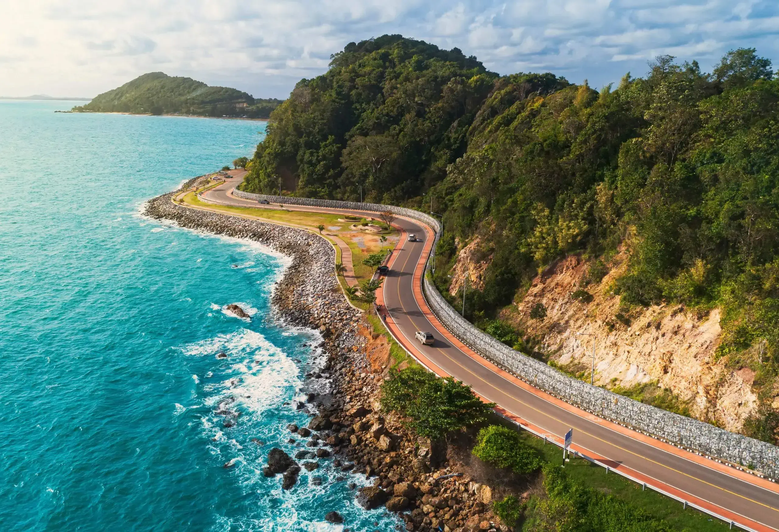 Cars travelling on a coastal road along the forested cliffs with vast ocean views.