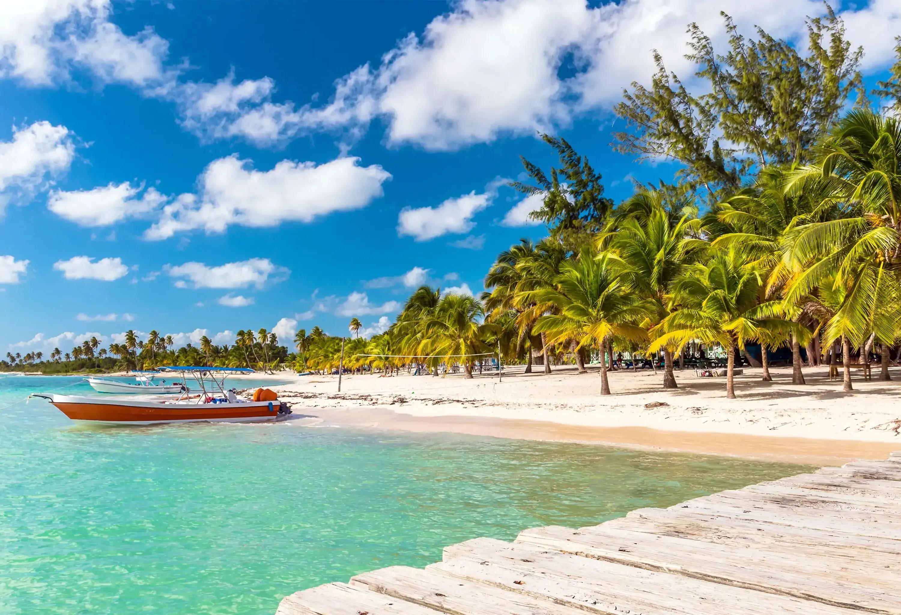 A tropical beach with boats gently moored nearby, swaying palm trees adorning the shore, and soft white sand inviting relaxation.