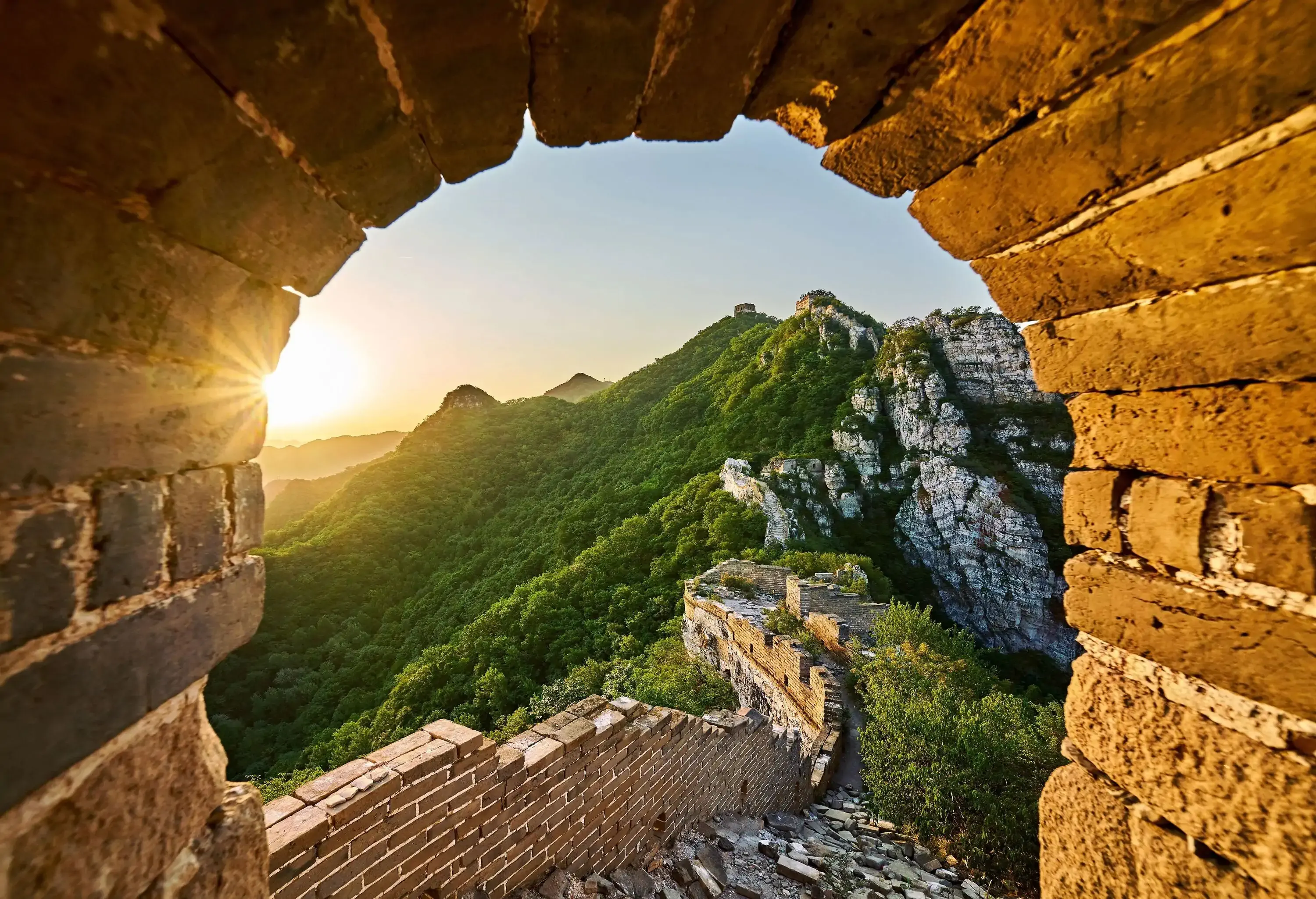 The majestic and historic Great Wall of China gracefully winds through lush foliage seen from a window.