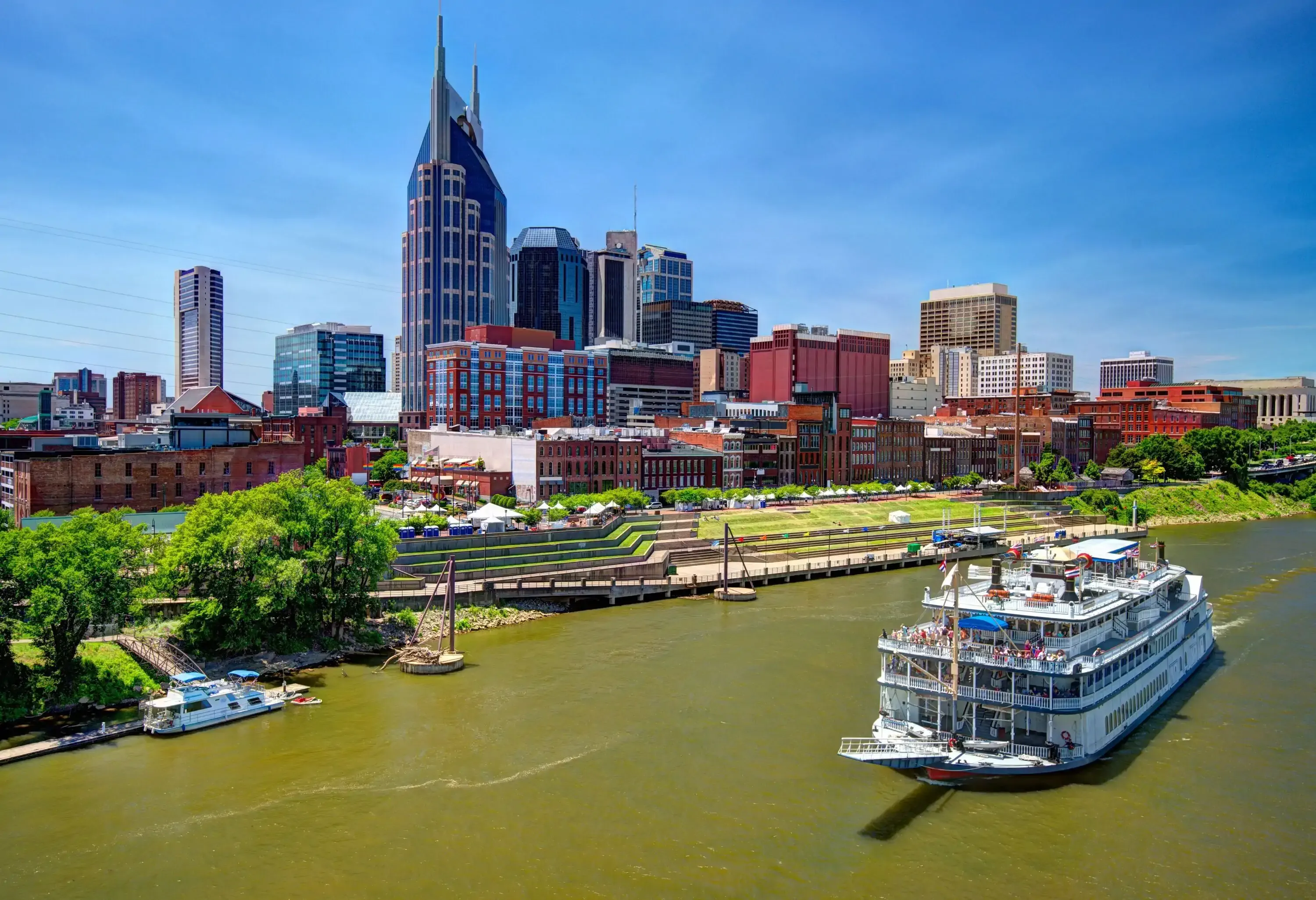 A big ferry boat cruising down a river, passing by the beautiful and tall architecture along the shore.