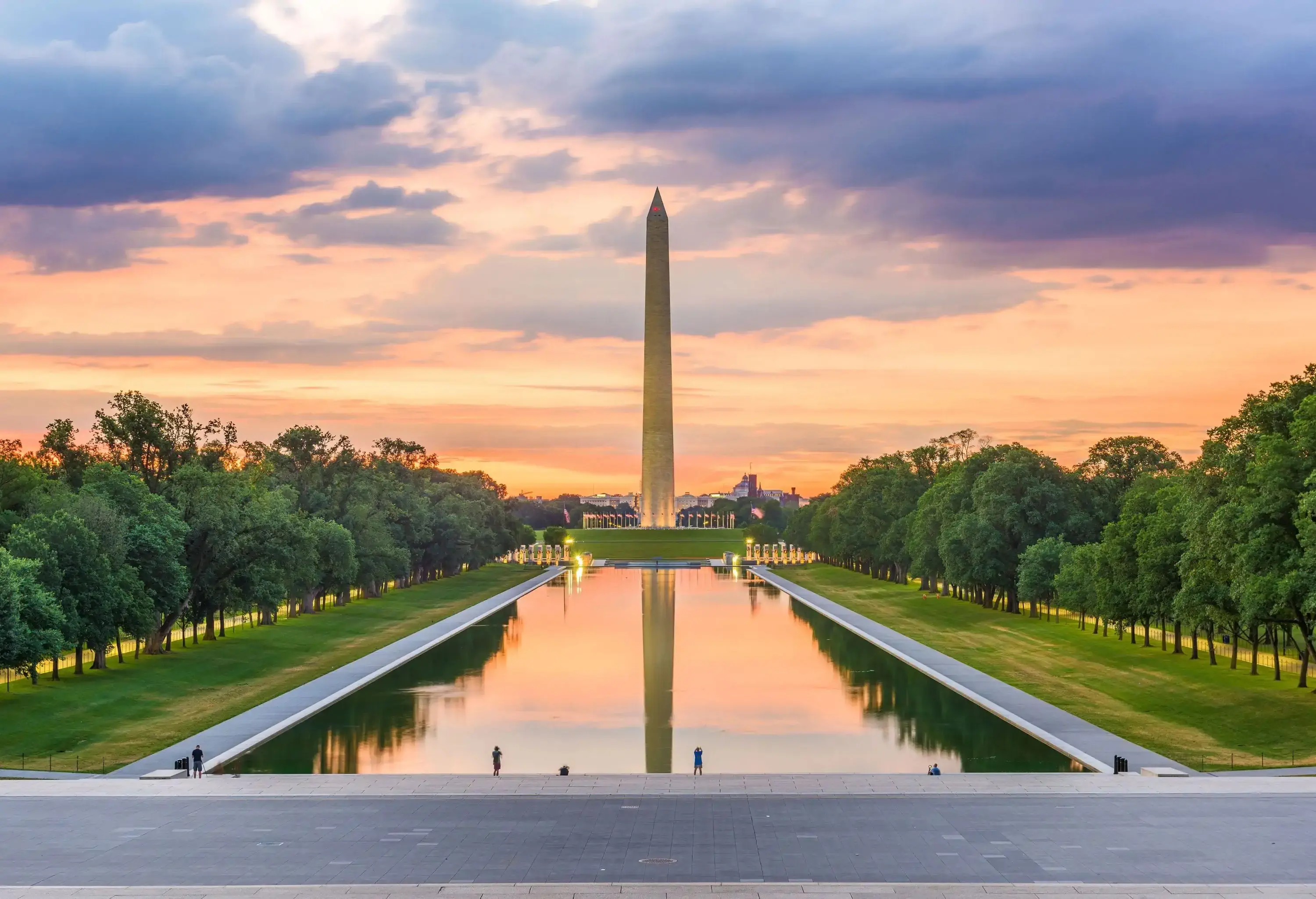 The iconic Washington Monument stands tall near a rectangular pool surrounded by lush trees.