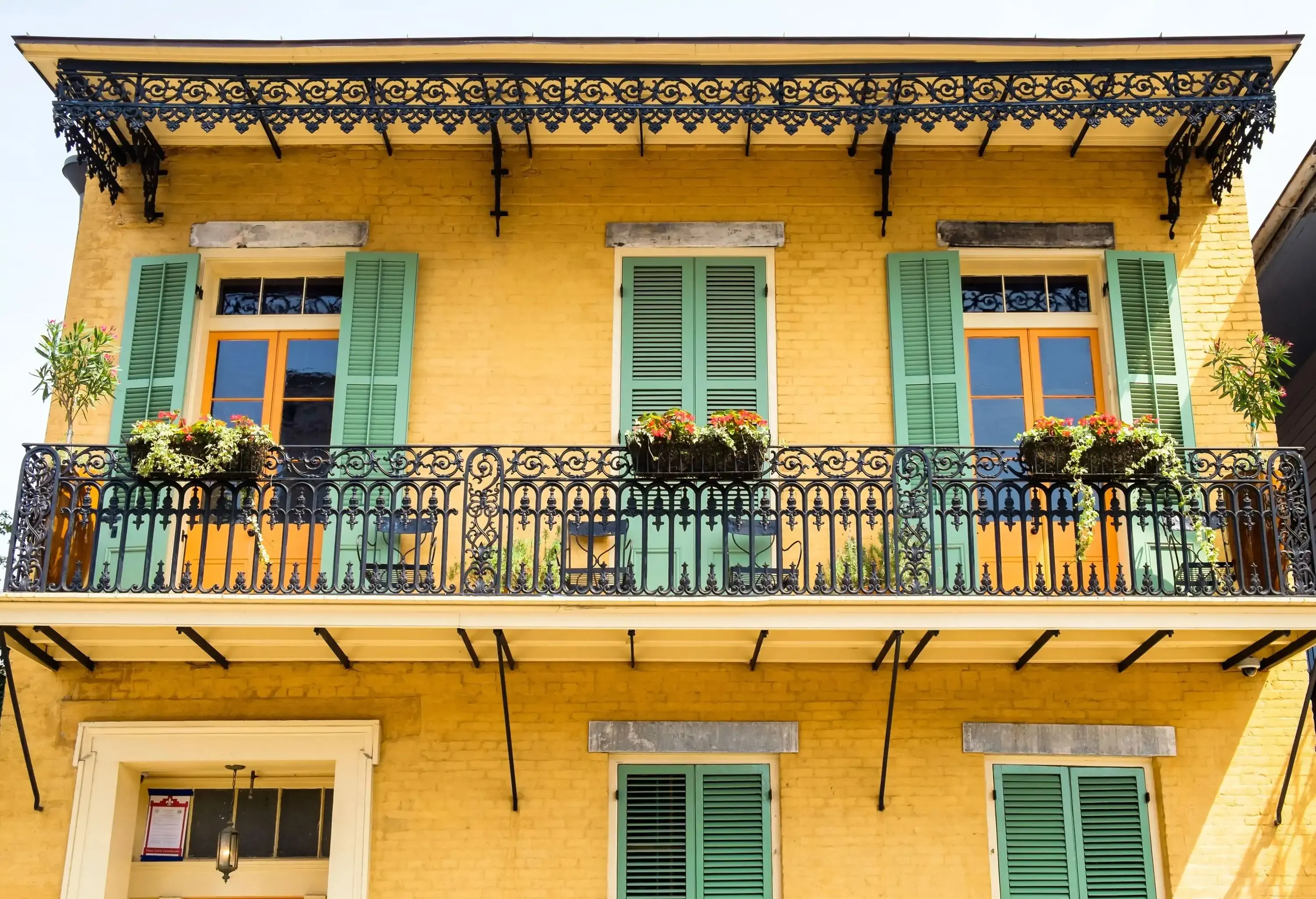 A yellow brick building, distinguished by its timeless charm, showcases intricate wrought iron rails on its balcony, embellished with plant potters that infuse natural beauty into its architectural allure.