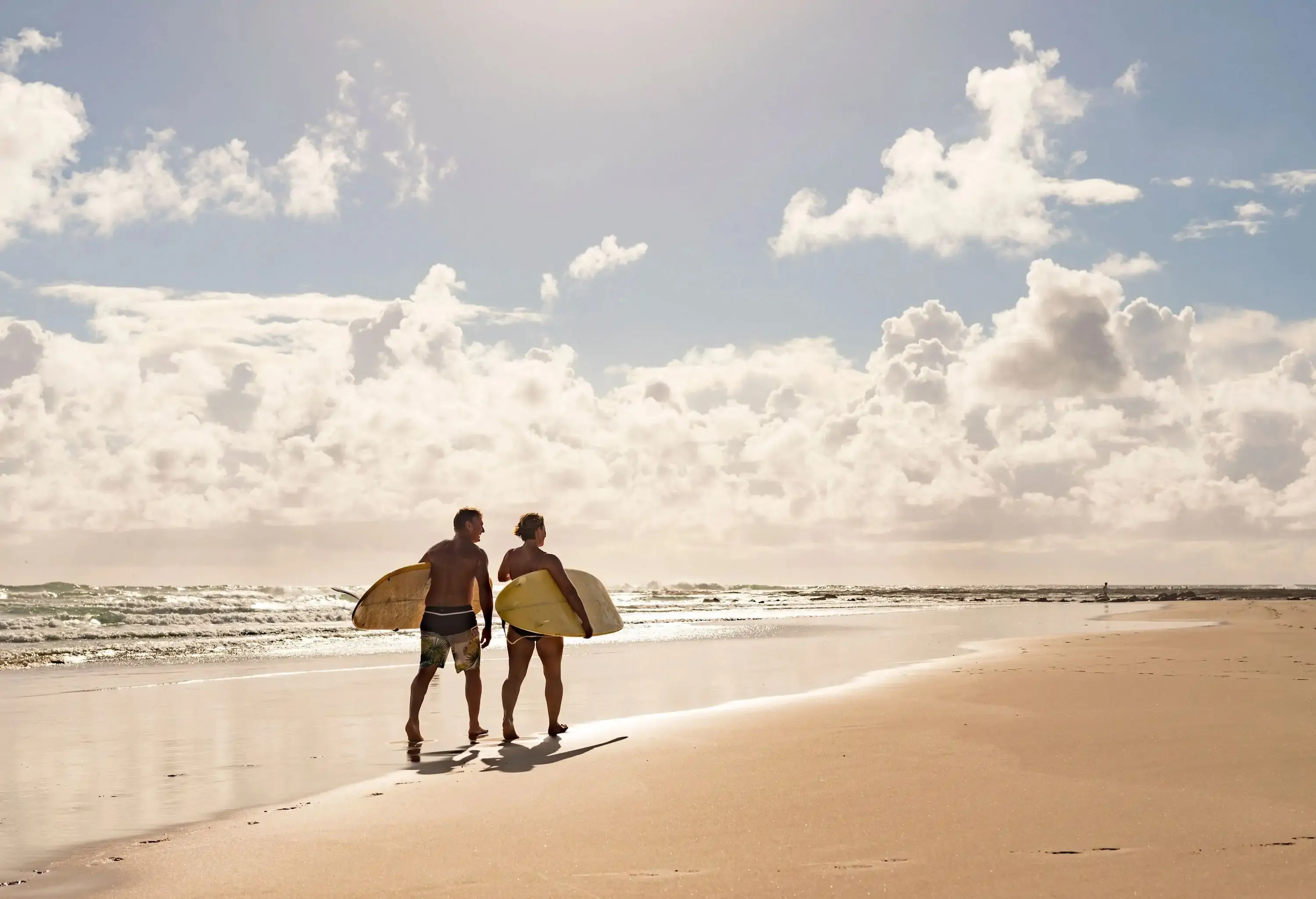 A couple carrying their surfboards walking along the beach on a sunny day.