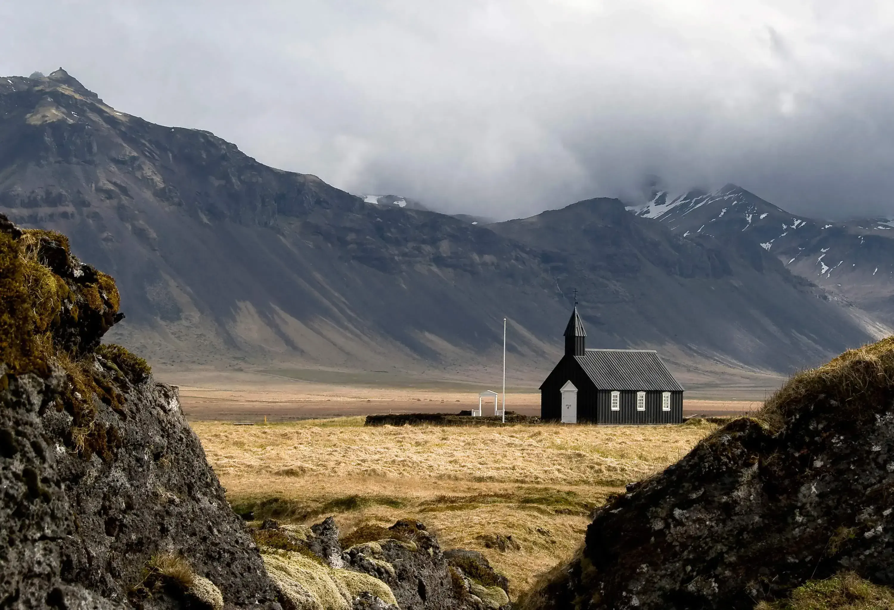 A wooden black church stands in a deserted field at the feet of a mountain