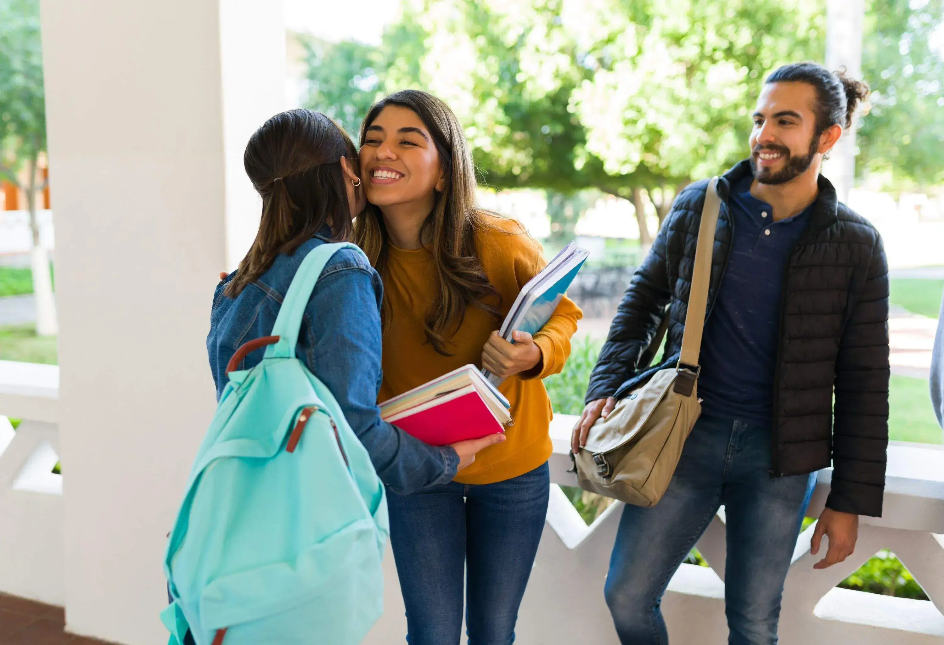 Happy young woman giving a kiss on the cheek to her best friend at the university while carrying books to class