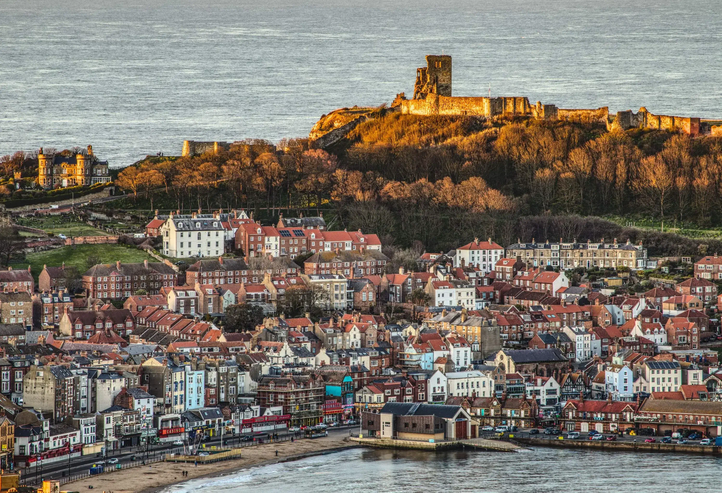 An old town across the coastline with a medieval fortress on a hill in the background.