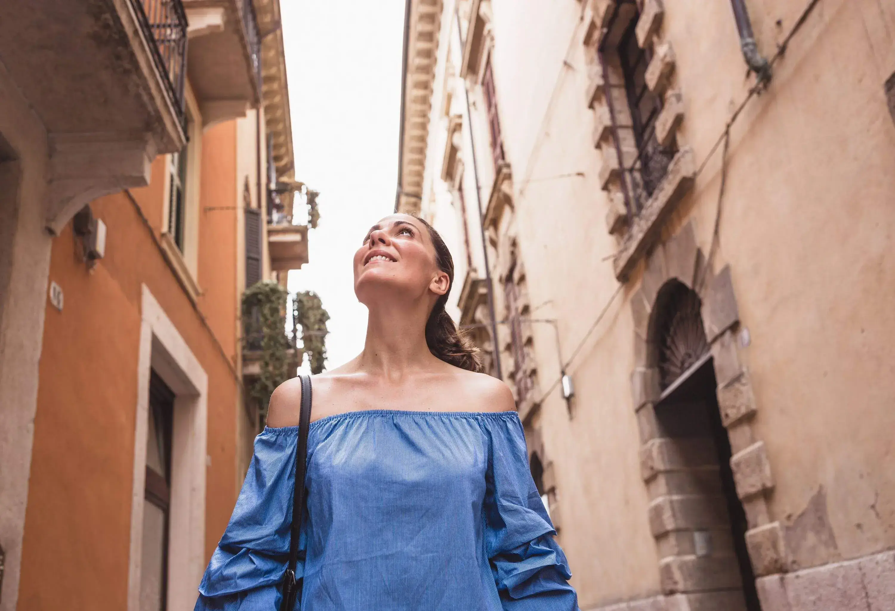 A lovely lady tourist wanders in an alleyway between the tall buildings.