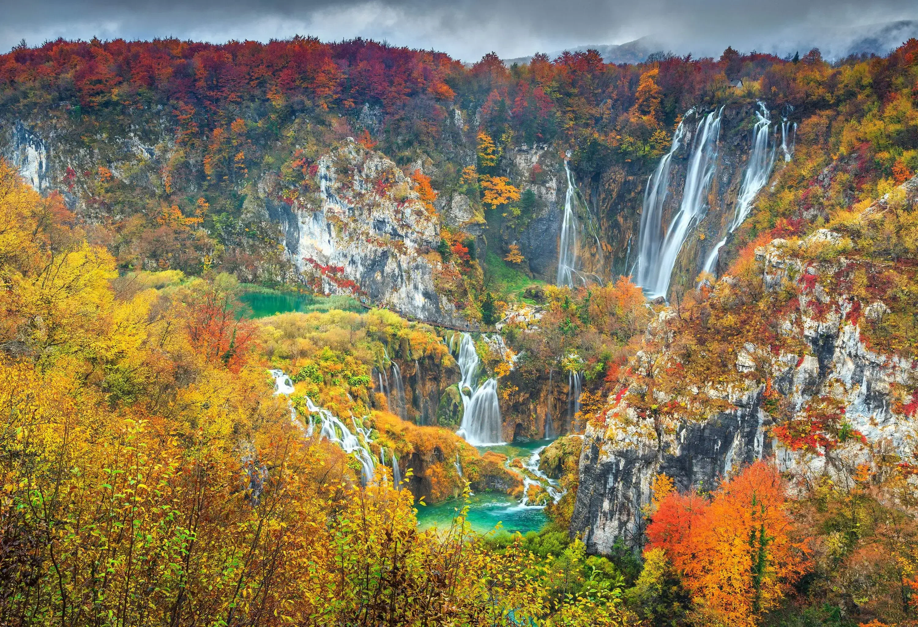Picturesque waterfalls with water gushing over the rocks into a river surrounded by rocky mountains covered with autumn trees.