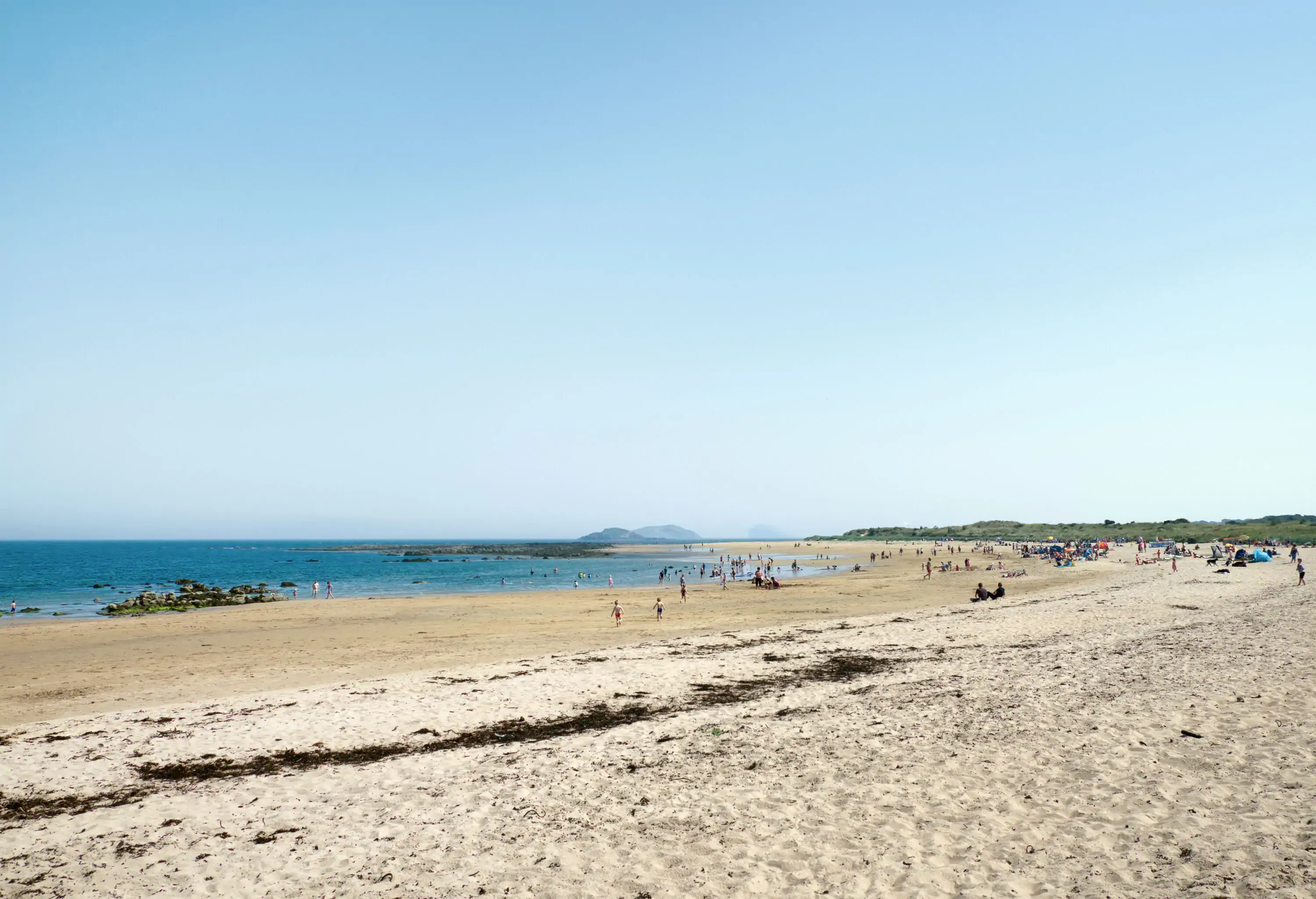 Wide beach in Scotland on a sunny day with people lounging in the sun