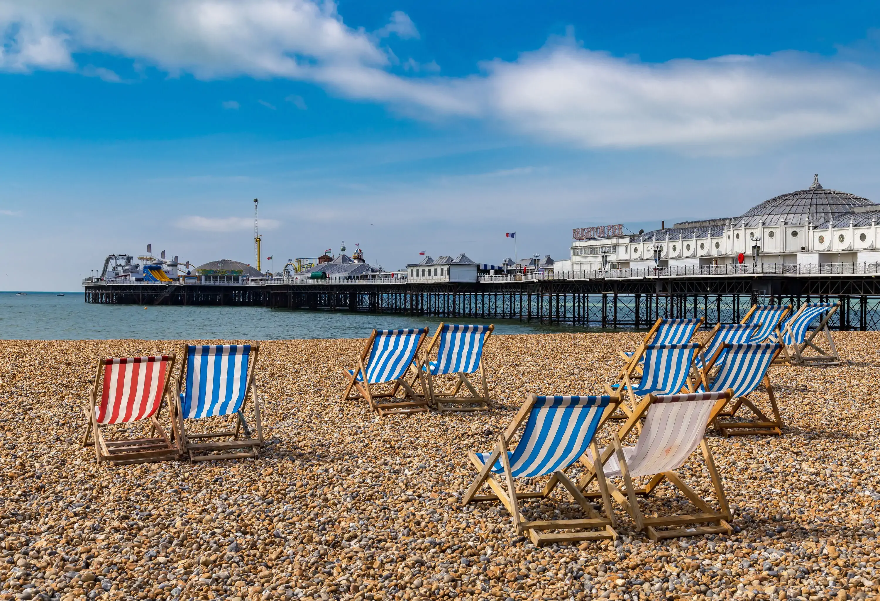 Colourful sunbeds with striped patterns set on a pebbled beach with views of an overwater pier.