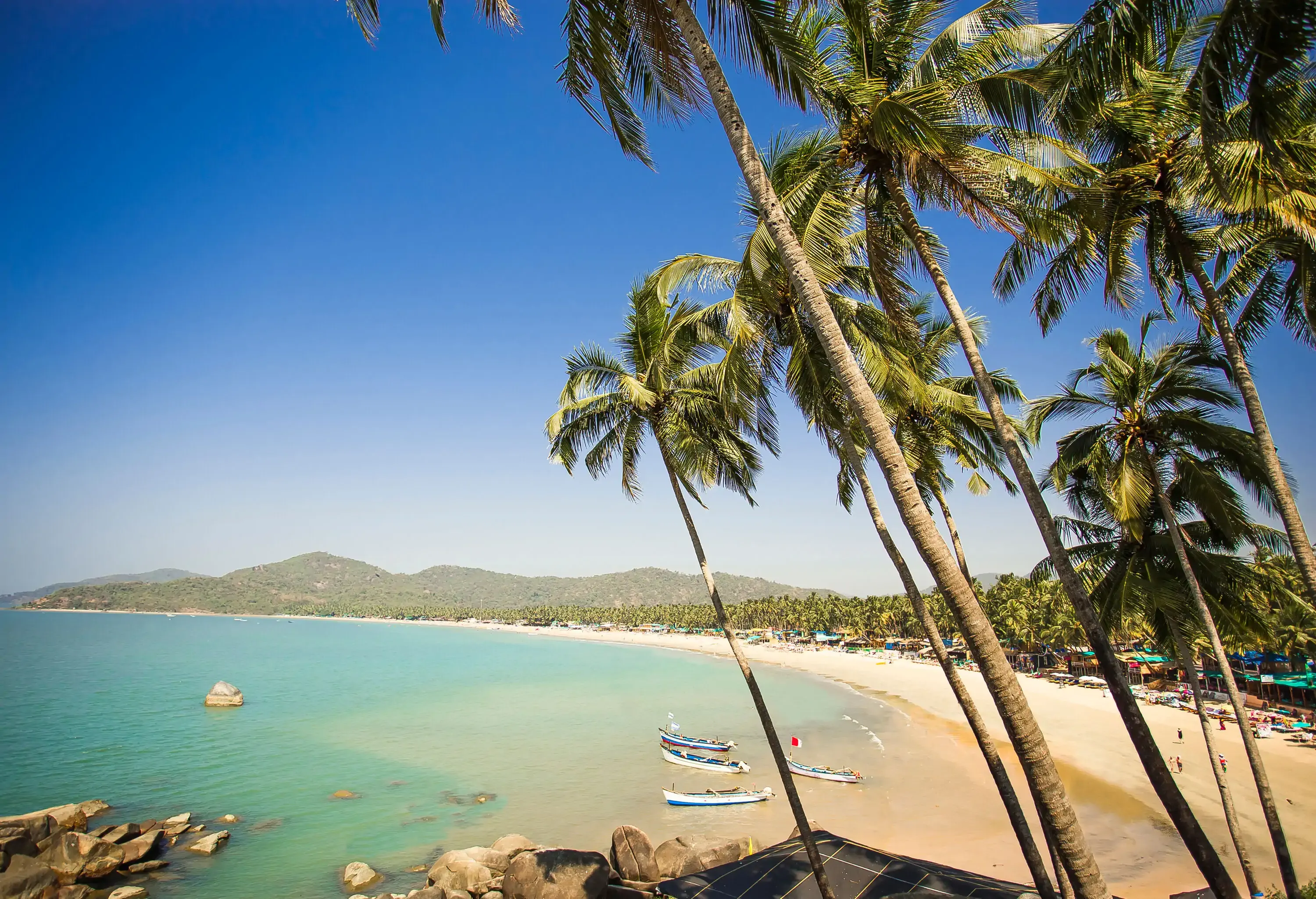 A long stretch of white sand beach surrounds the turquoise bay on a cloudless sky.