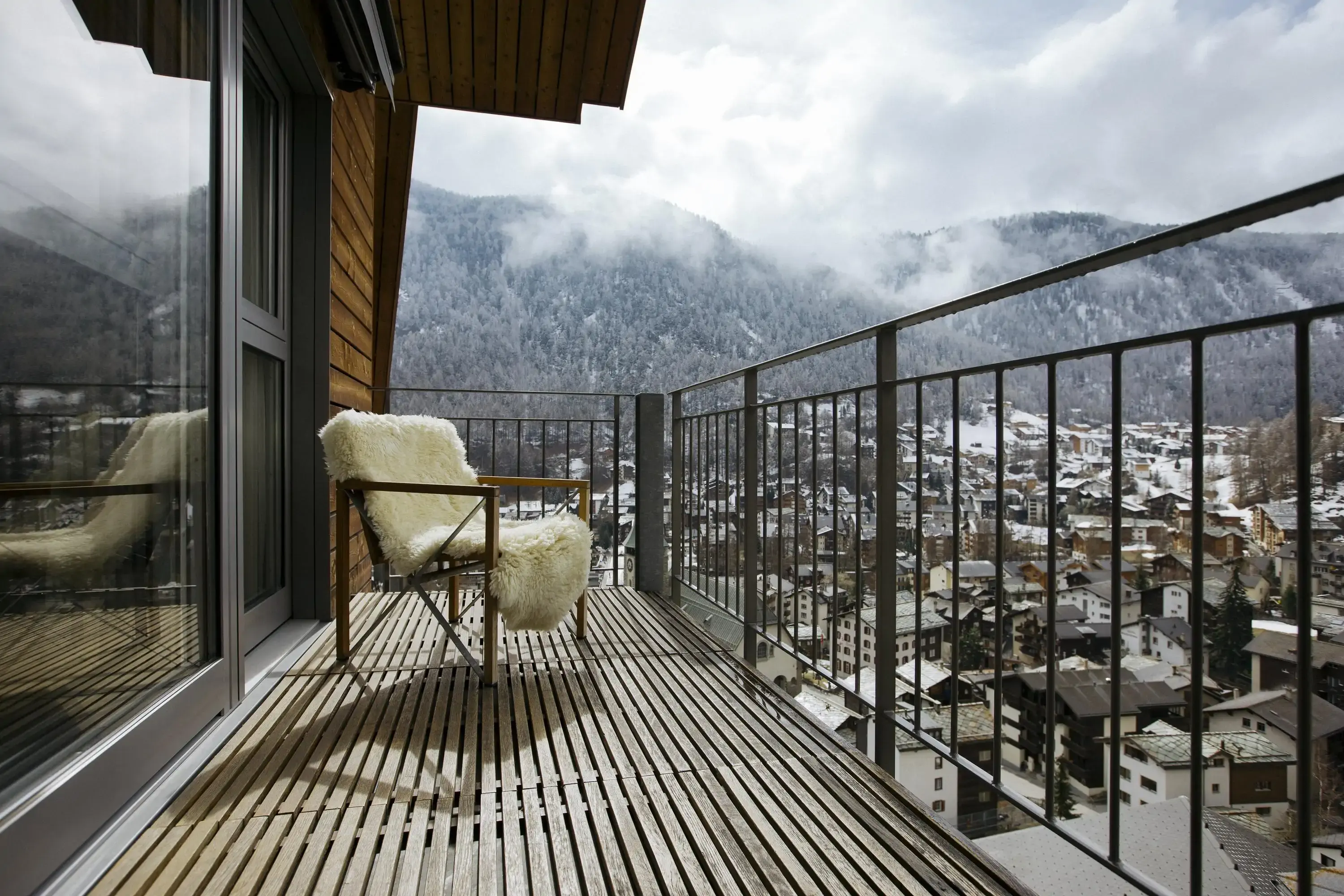 Low angle view of a chair covered in a sheepskin rug on a balcony overlooking a snow-covered Alpine village